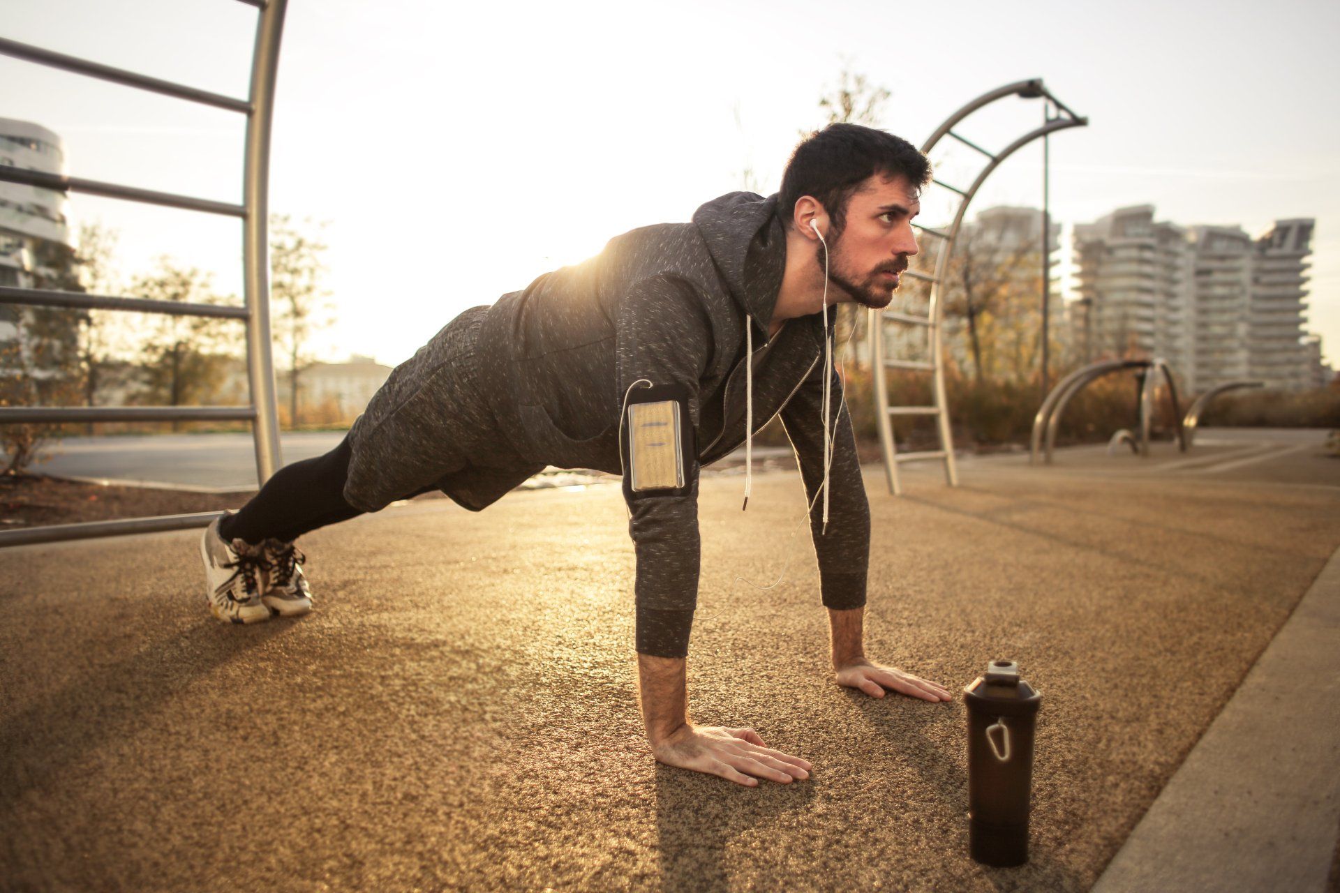 Man doing a plank exercise outdoors at sunset beside a water bottle