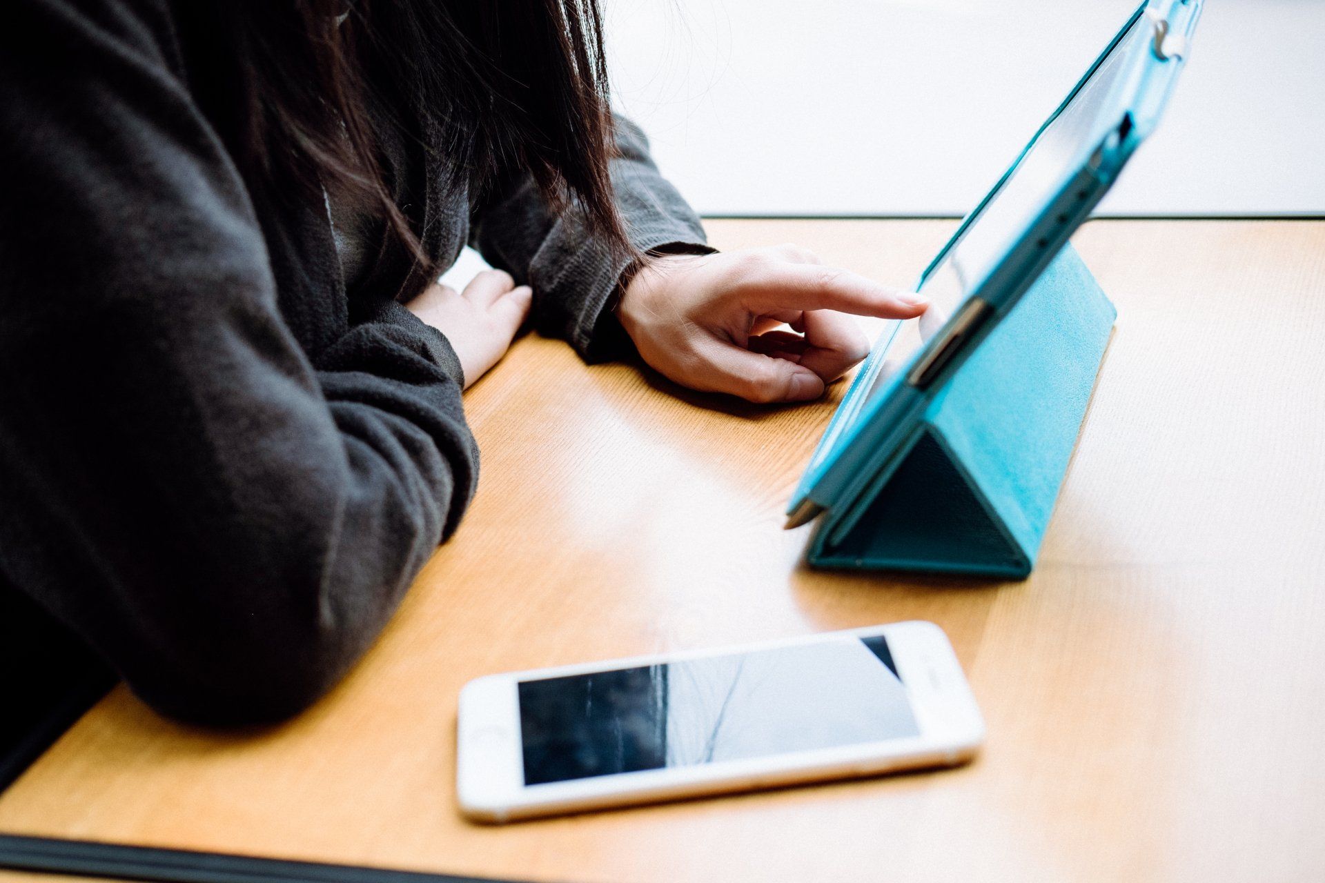 A woman is sitting at a table using a tablet and a cell phone.