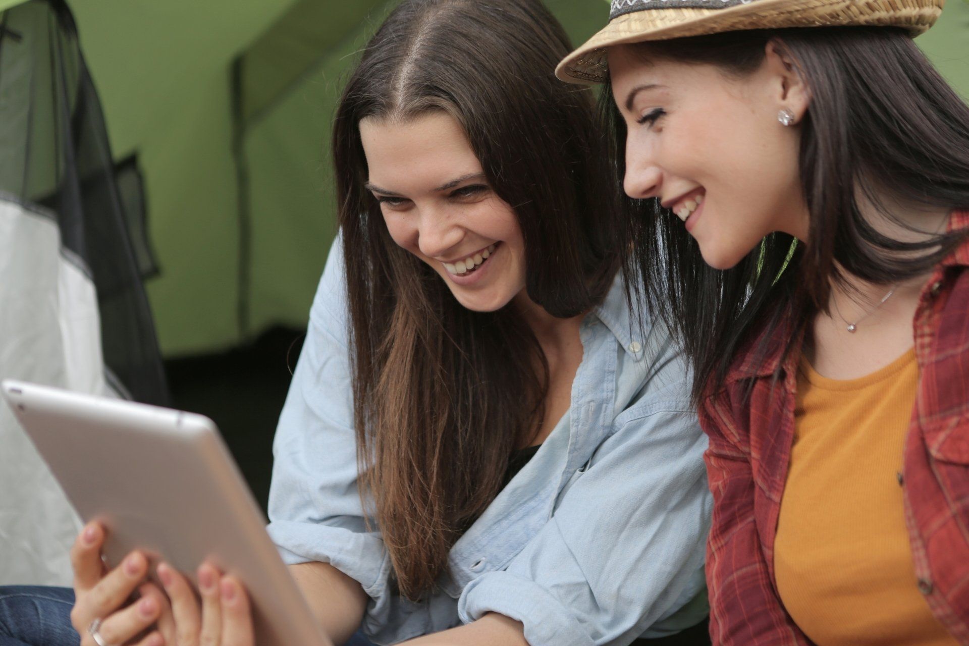 Two women are sitting in front of a tent looking at a tablet.
