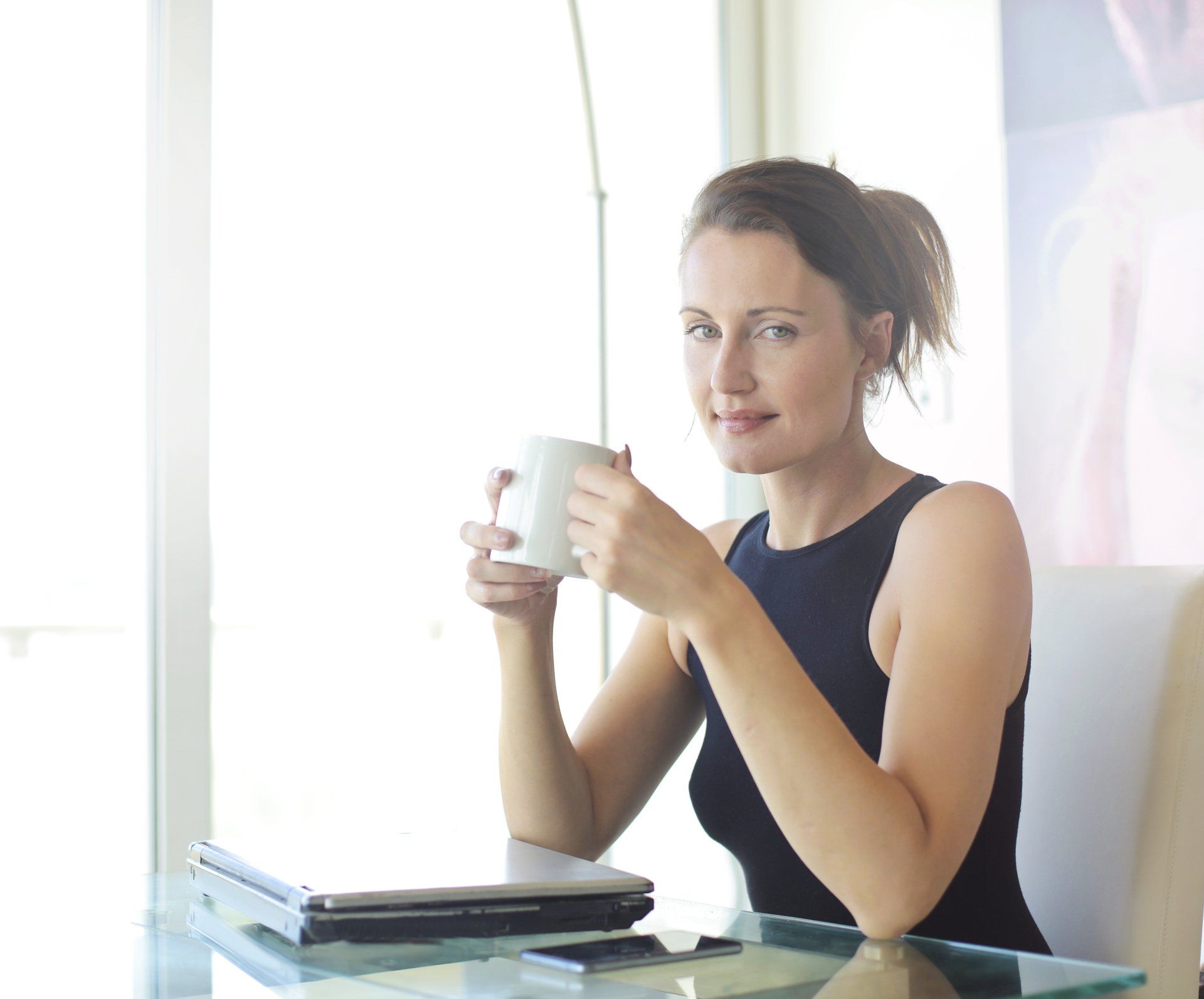 A woman is sitting at a table drinking a cup of coffee