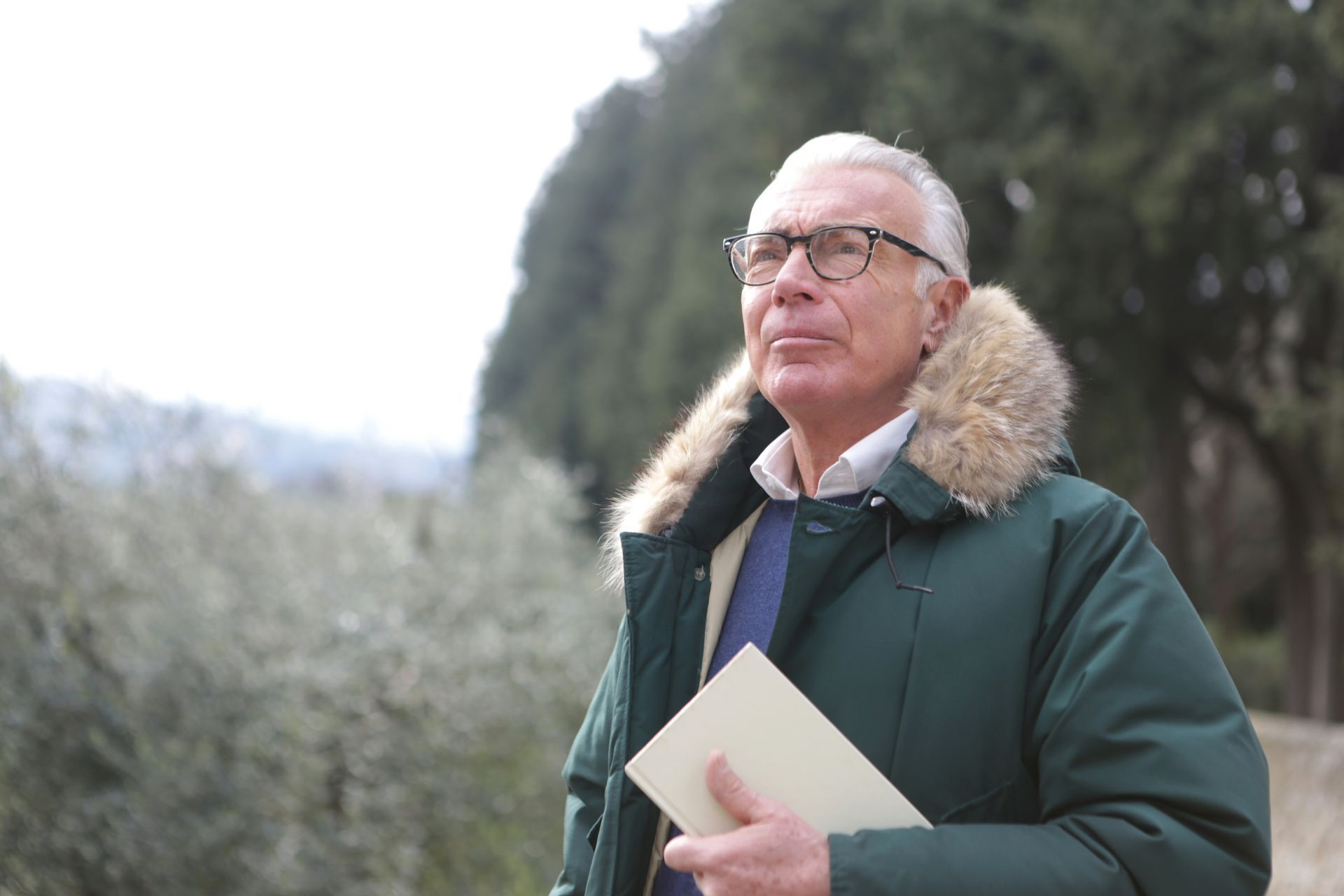 A man in a green jacket and glasses is holding a piece of paper.