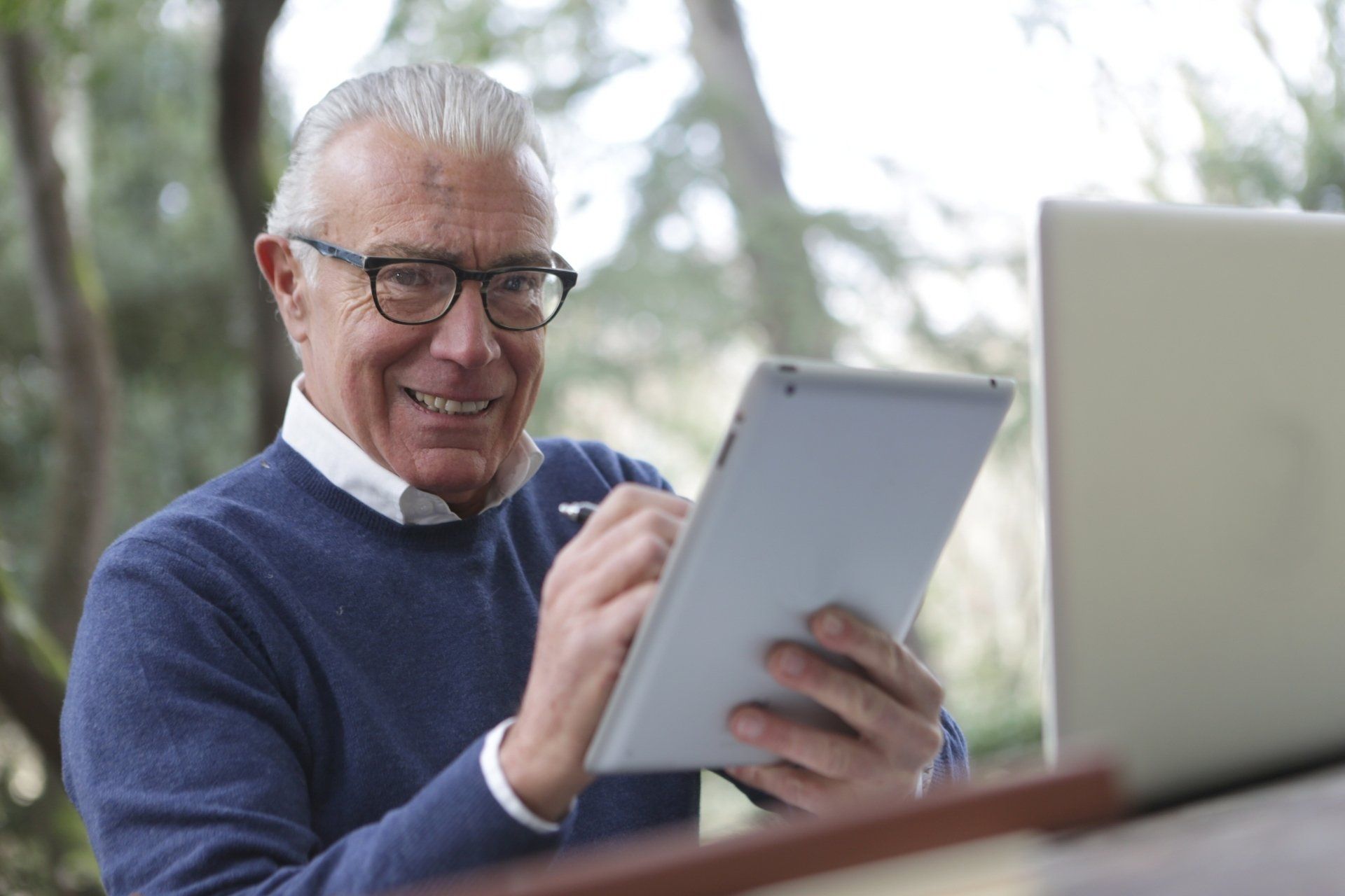 An older man is using a tablet computer in front of a laptop computer.