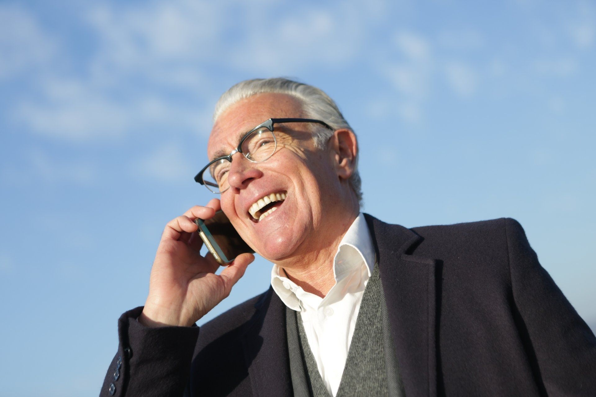 Smiling man in suit talking on a cellphone outdoors against a blue sky
