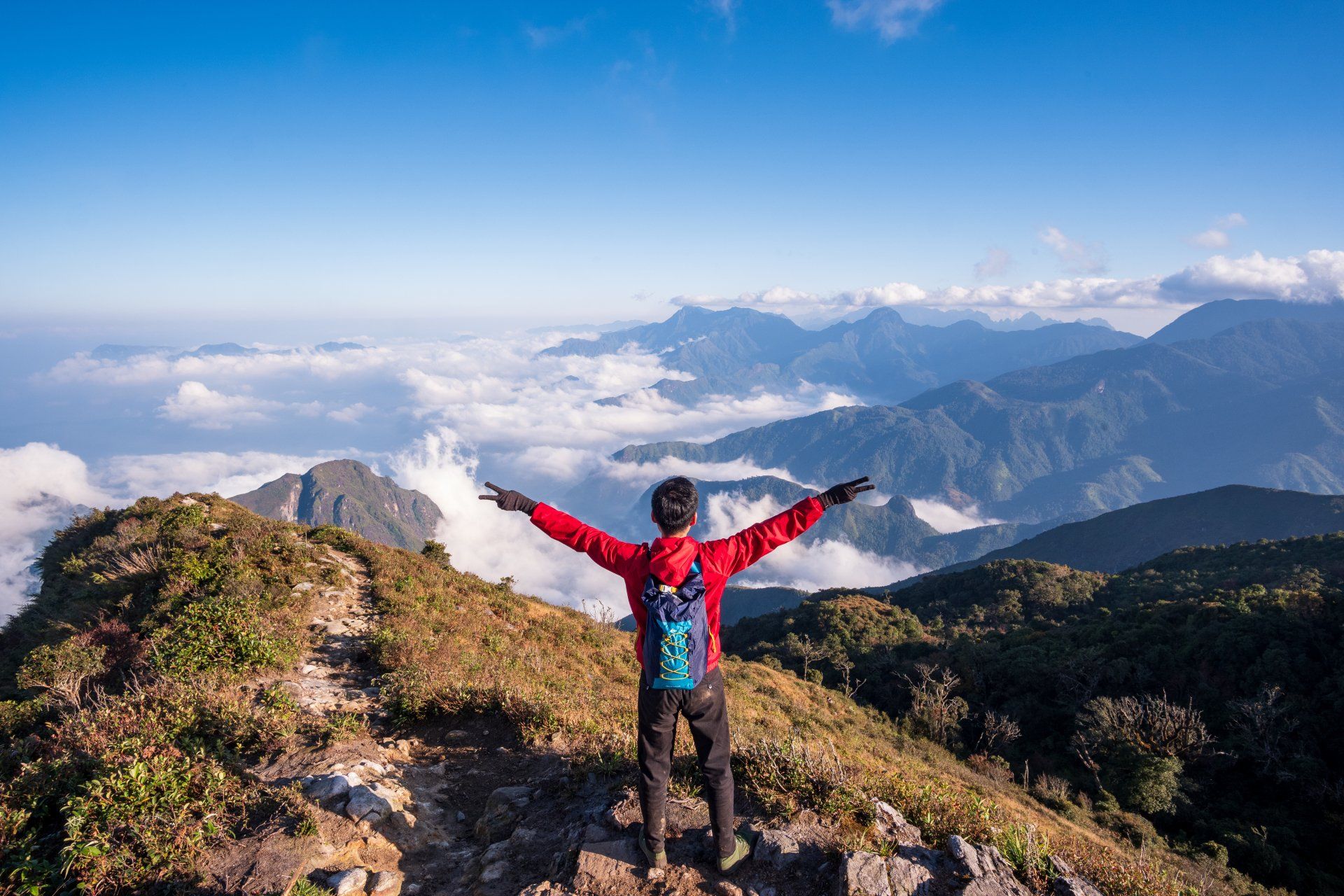 A man is standing on top of a mountain with his arms outstretched.