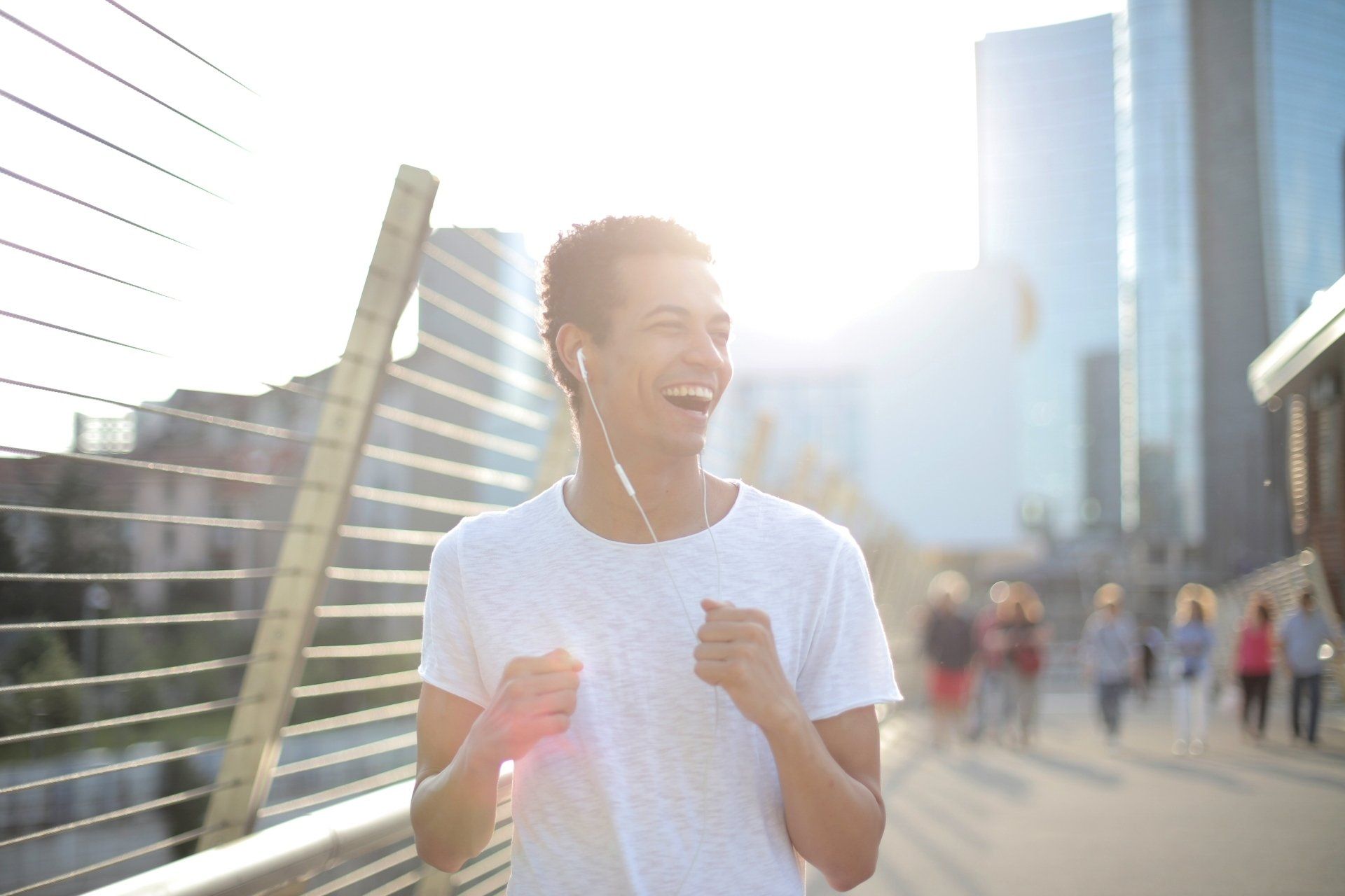 A man wearing headphones running on a bridge in the city.