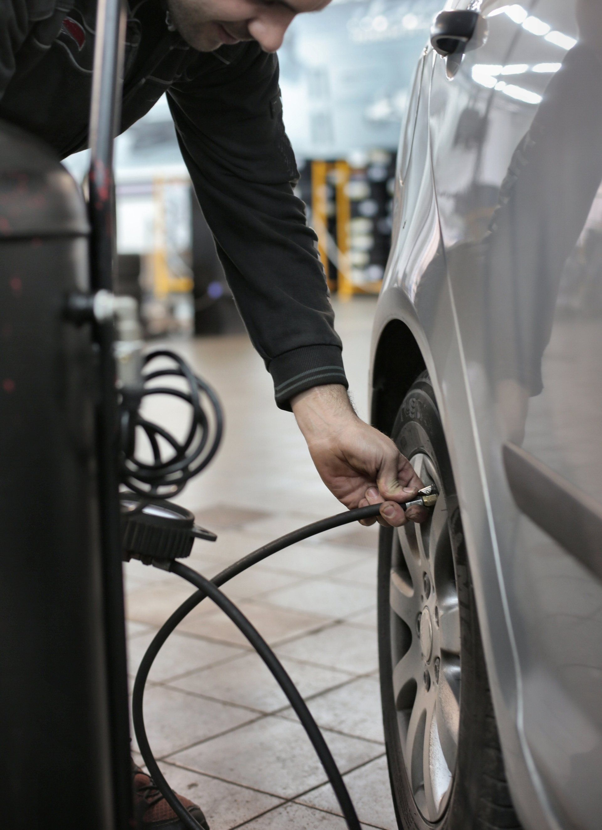 Person inflating a car tire with an air compressor in a garage.