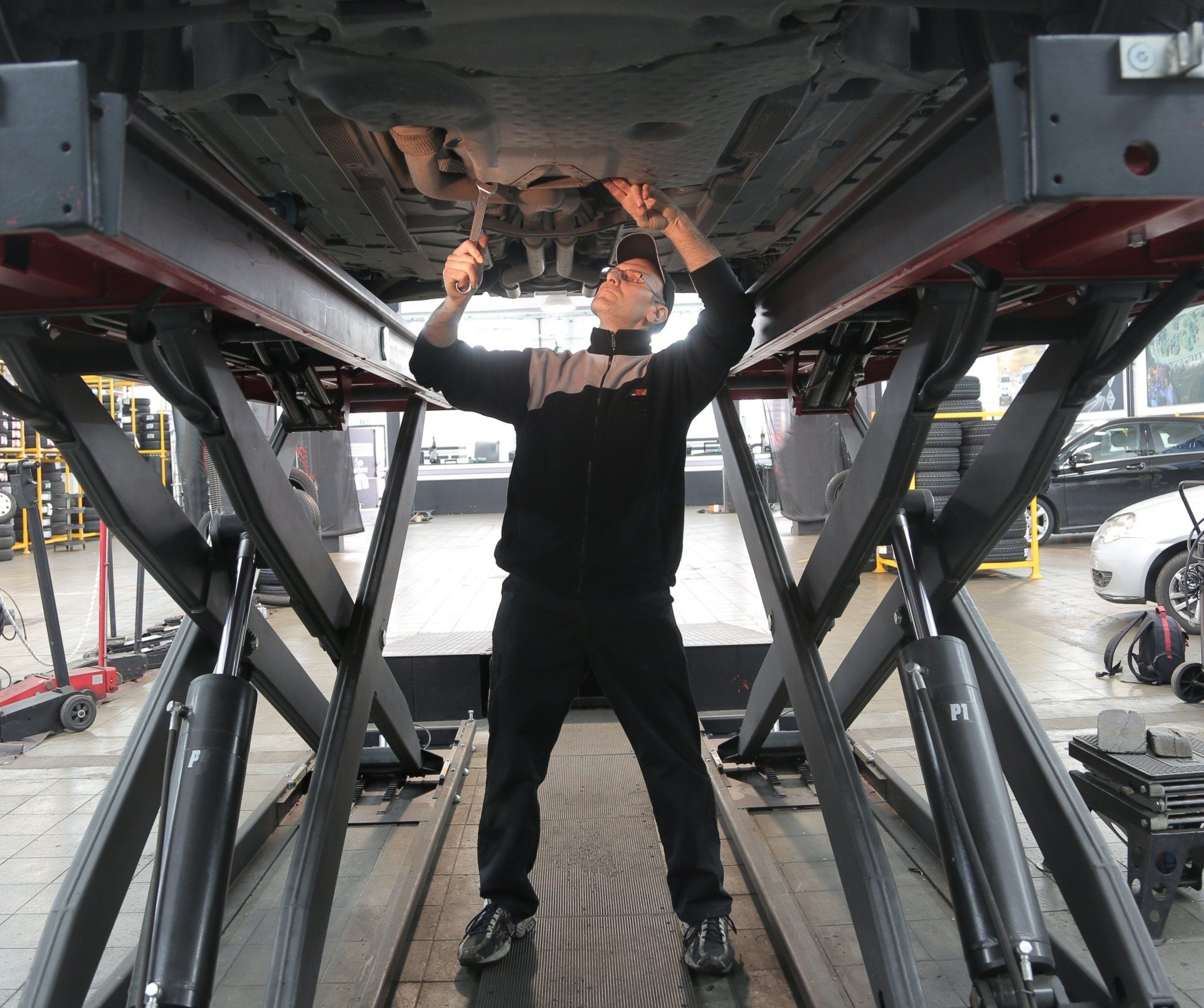 Mechanic working under a car lifted on a hydraulic platform in a garage, using a wrench.