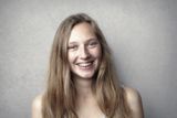 Woman with long, light brown hair, smiles broadly, wearing braces against a gray background.