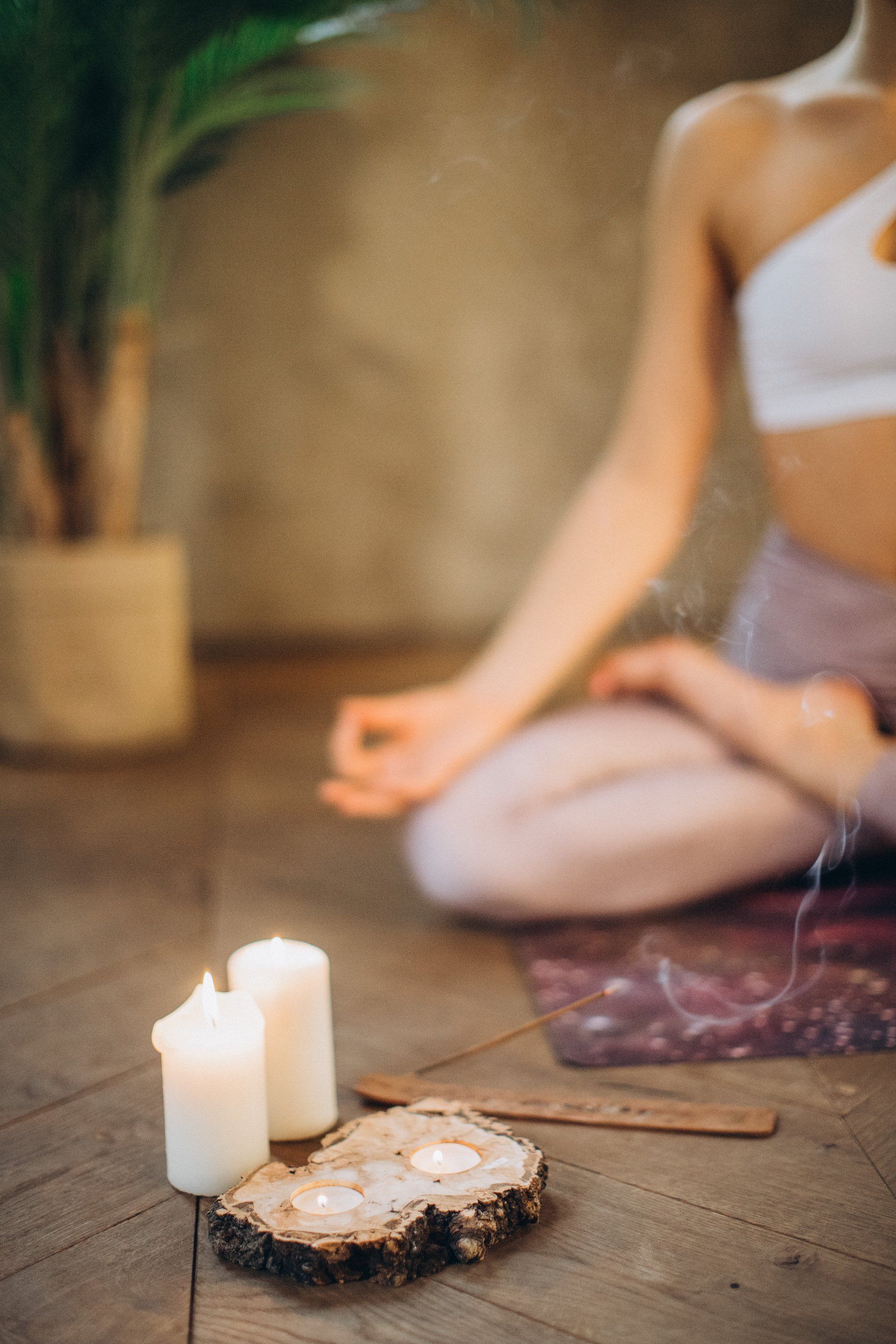 Vrouw mediteert met kaarsen, wierook en een plant in een schemerig verlichte kamer.