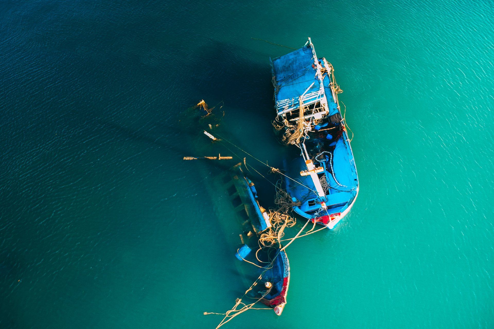 Overhead view of a blue boat and debris floating in turquoise water