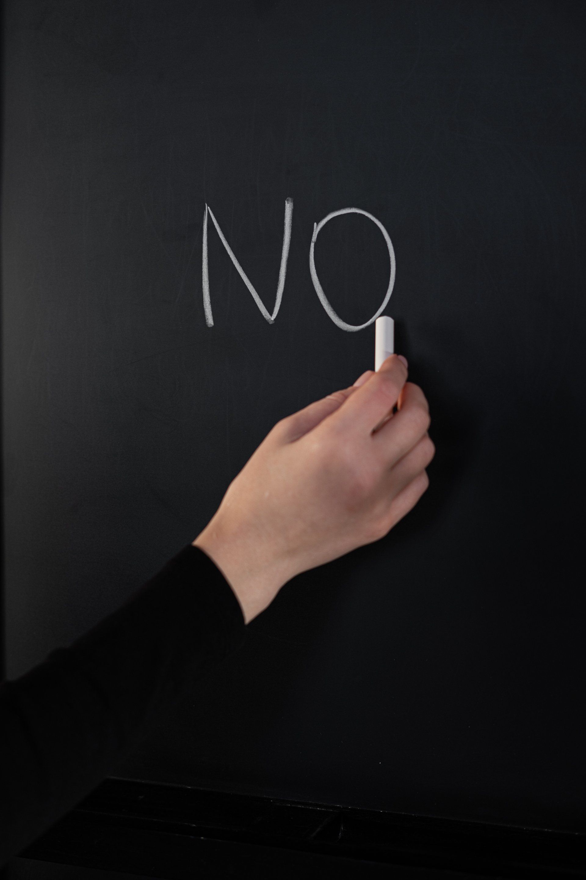 A person is writing the word no on a blackboard