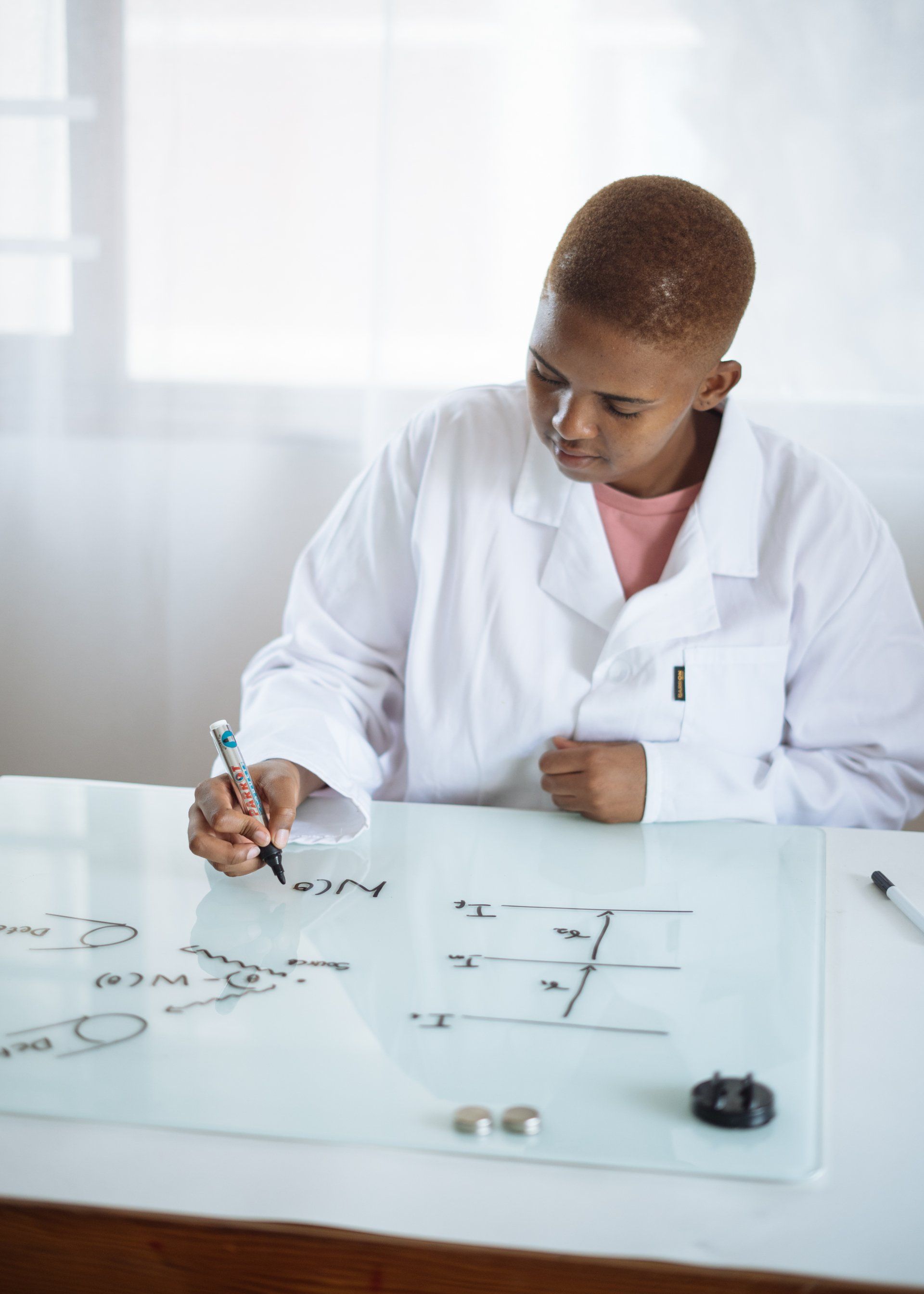 A woman in a lab coat is writing on a whiteboard.