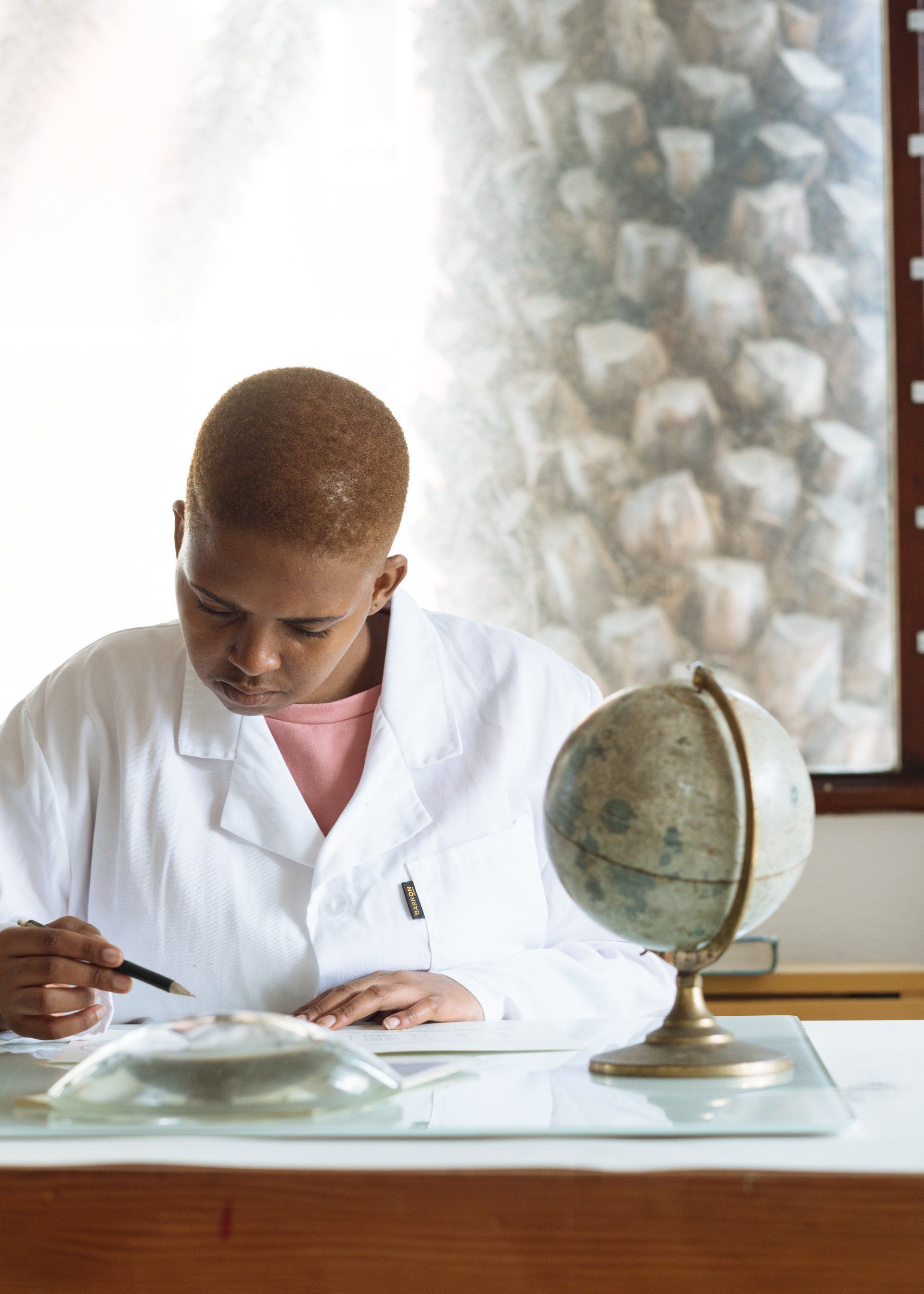 A woman in a lab coat is sitting at a desk with a globe on it.