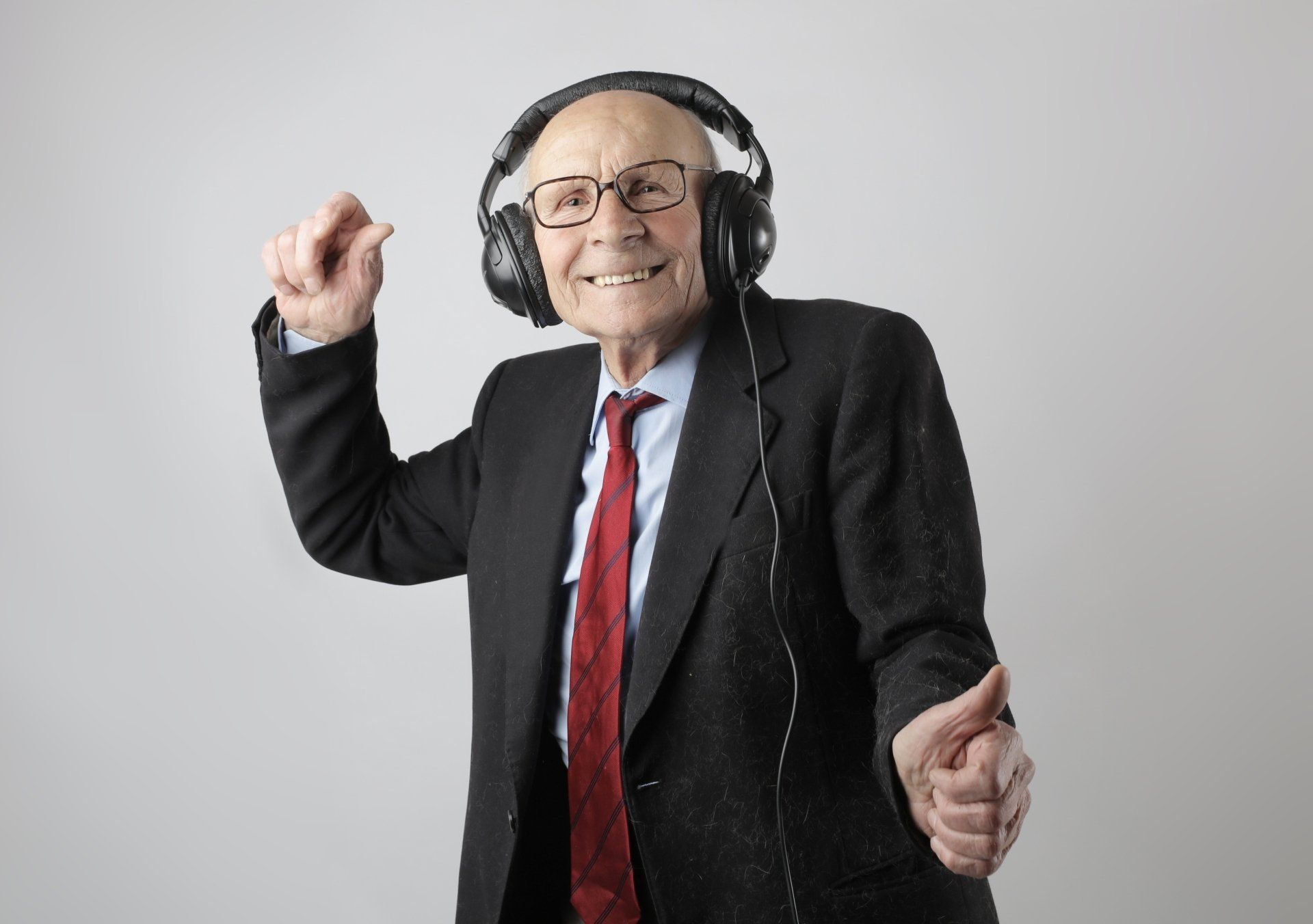 An elderly man in a suit and tie is wearing headphones and dancing.