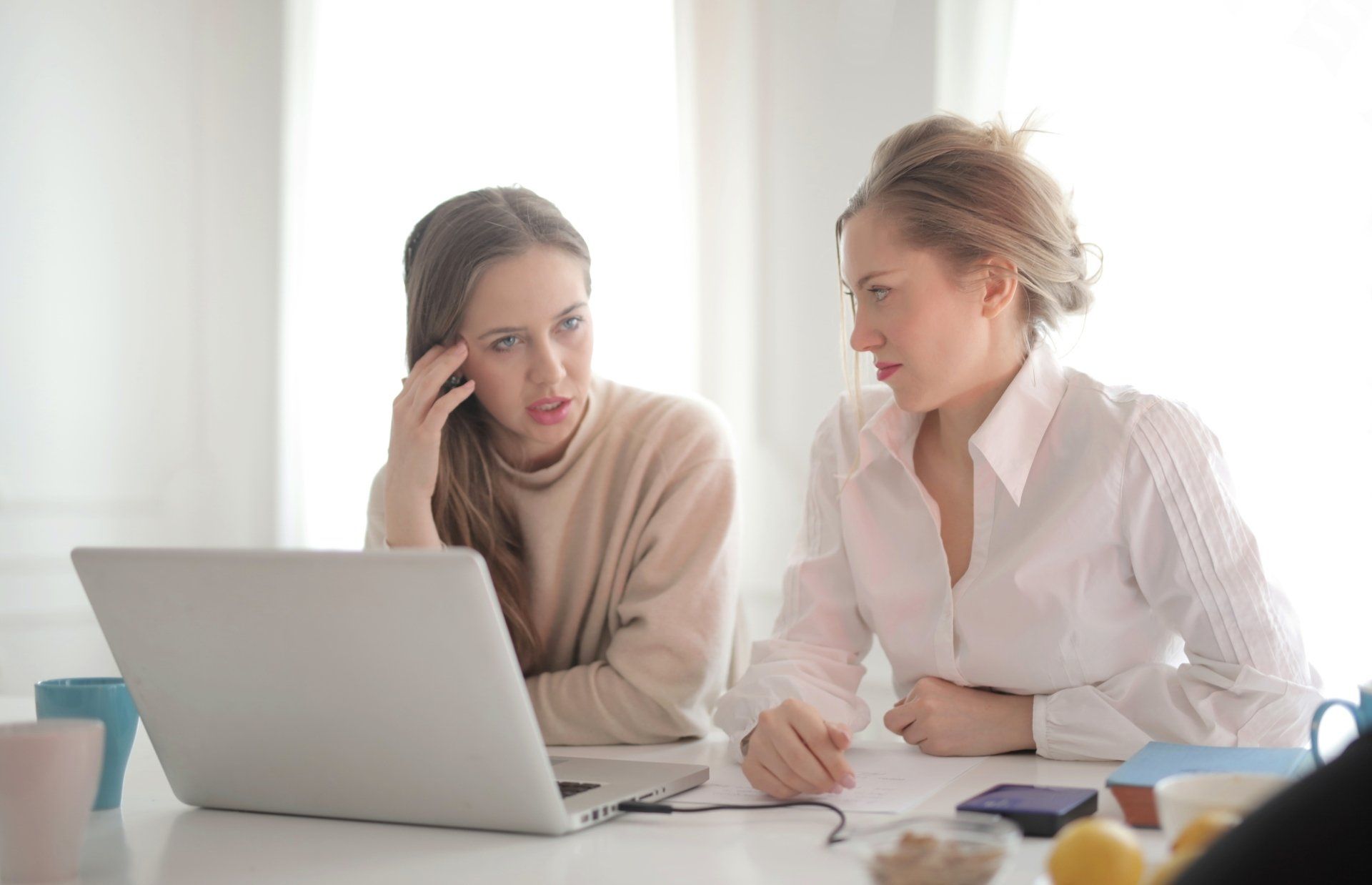 Two women are sitting at a table looking at a laptop computer.