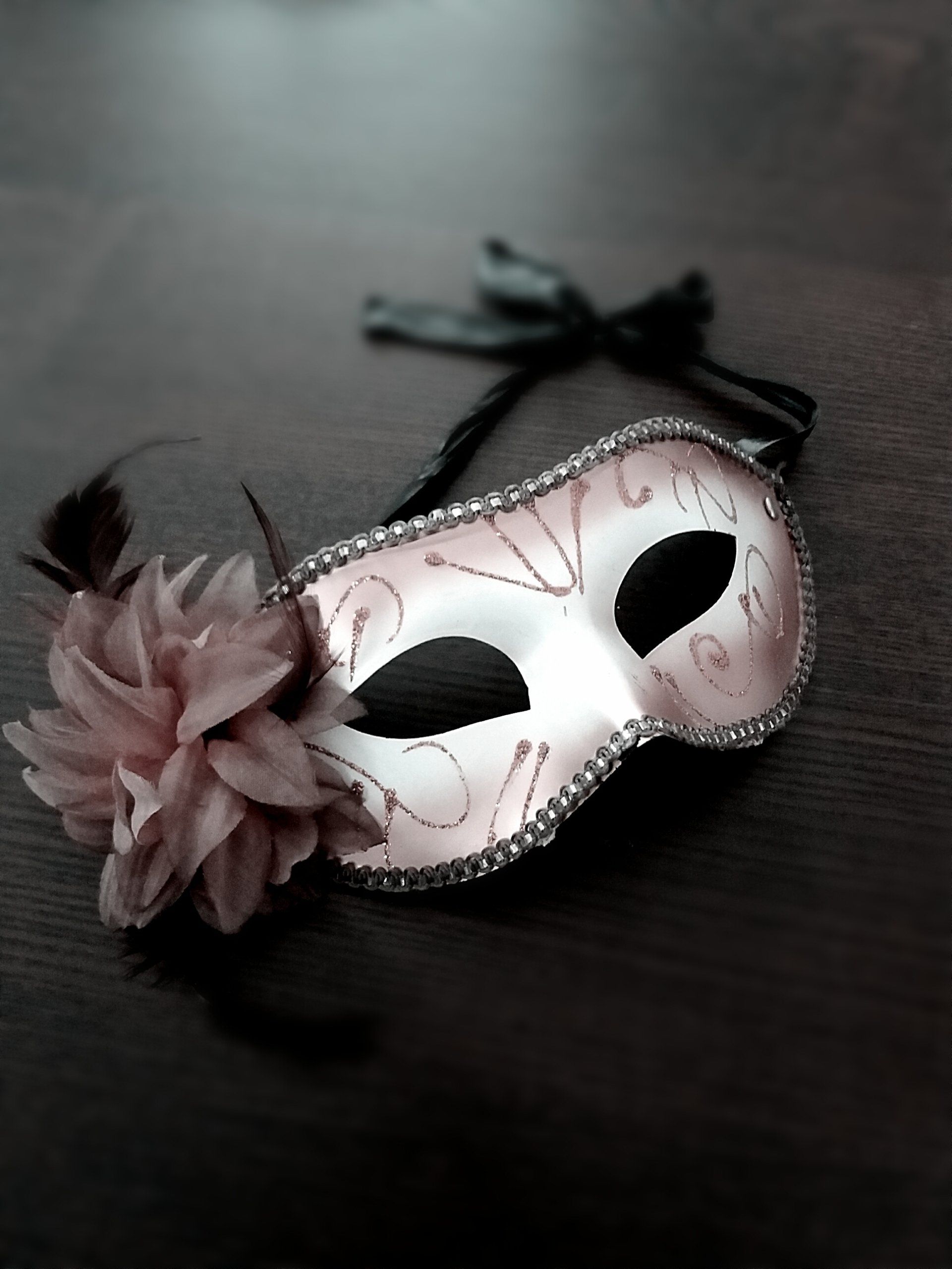 Wäiss Maskenballmask mat rosa Blummen op engem donkelen Hannergrond