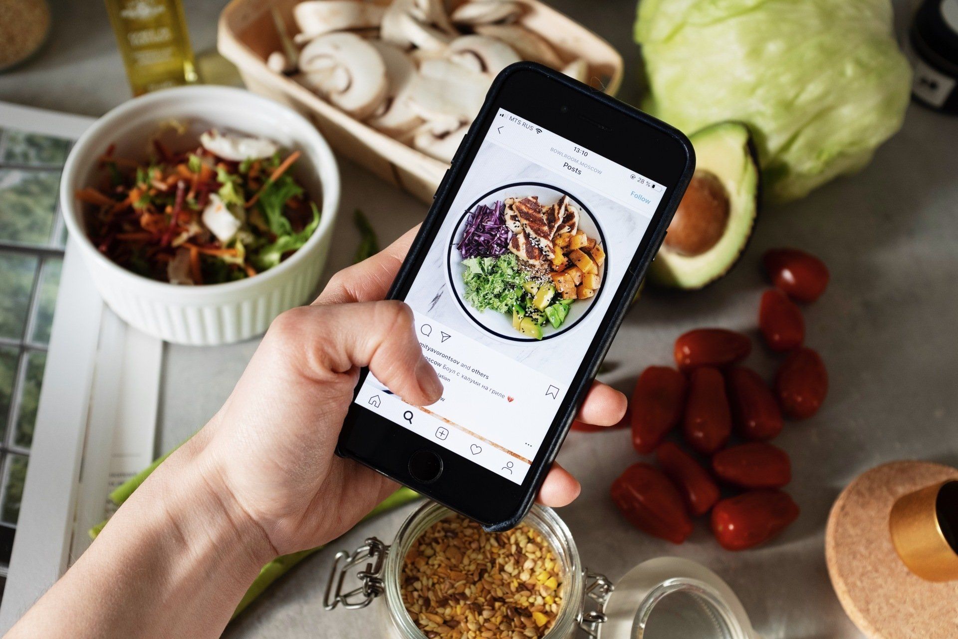 A person is holding a cell phone with a picture of a salad on the screen.