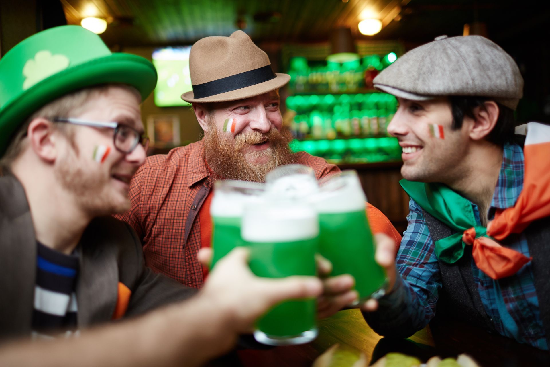 Three men in a pub toasting with green beer; St. Patrick's Day celebration, green and orange accents, smiling faces.