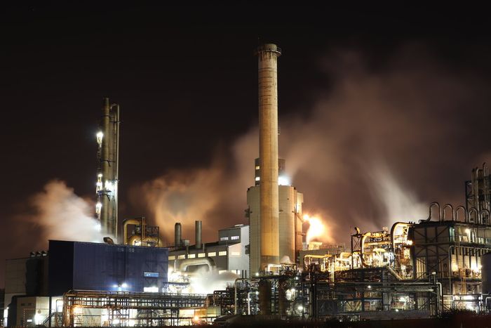Night view of an industrial plant with smokestacks emitting steam and lights illuminating machinery against a dark sky.