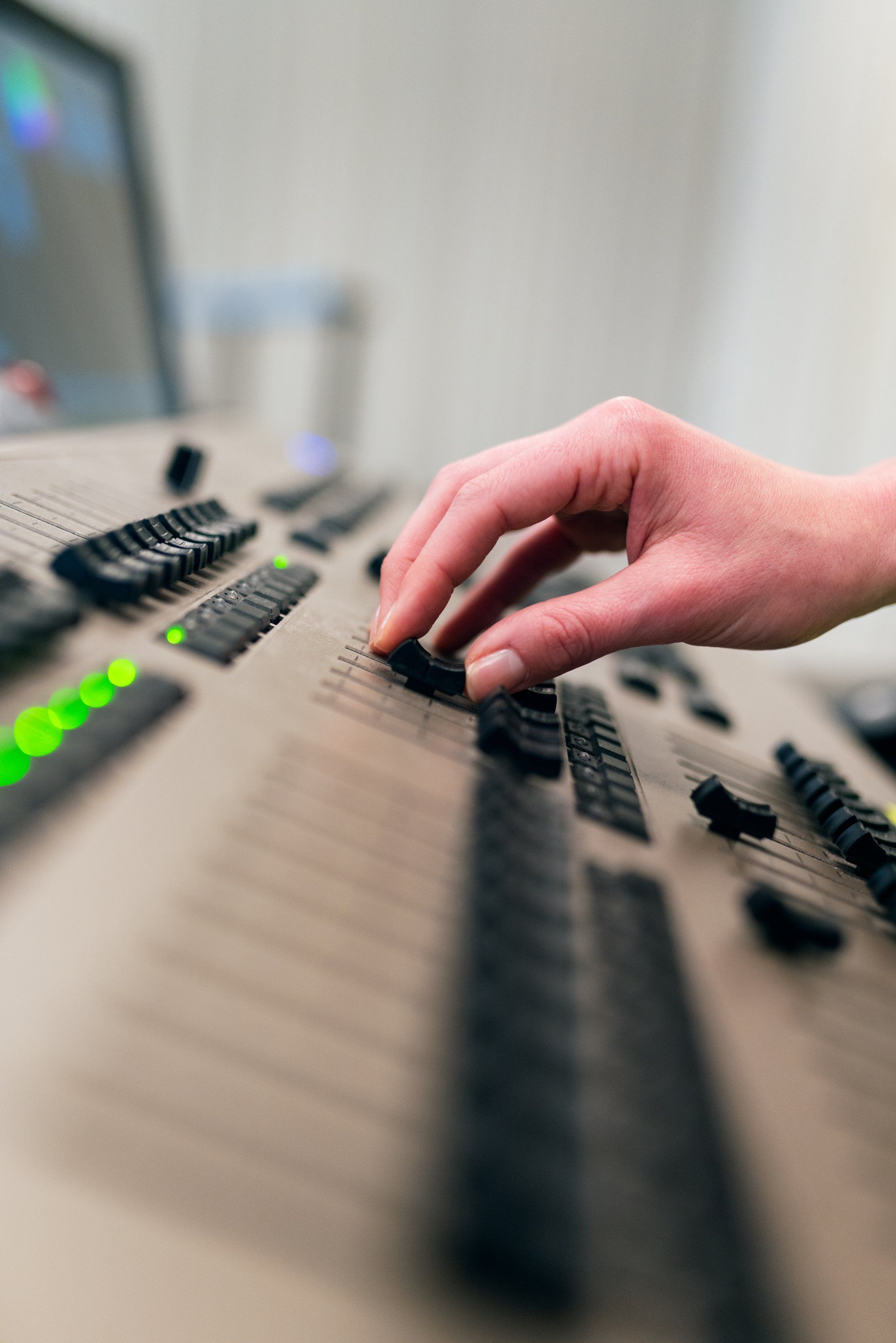 Hand adjusting fader on a sound mixing console with various controls and lights.