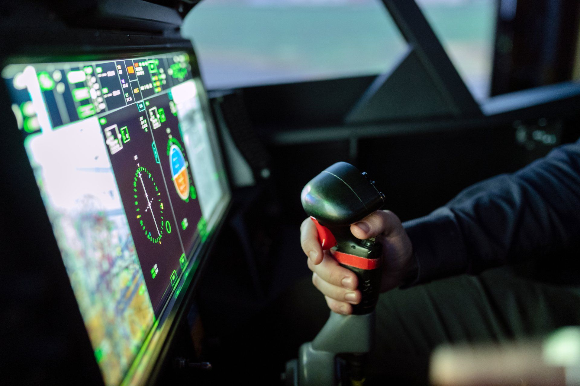 A person is holding a joystick in front of a monitor in a cockpit.