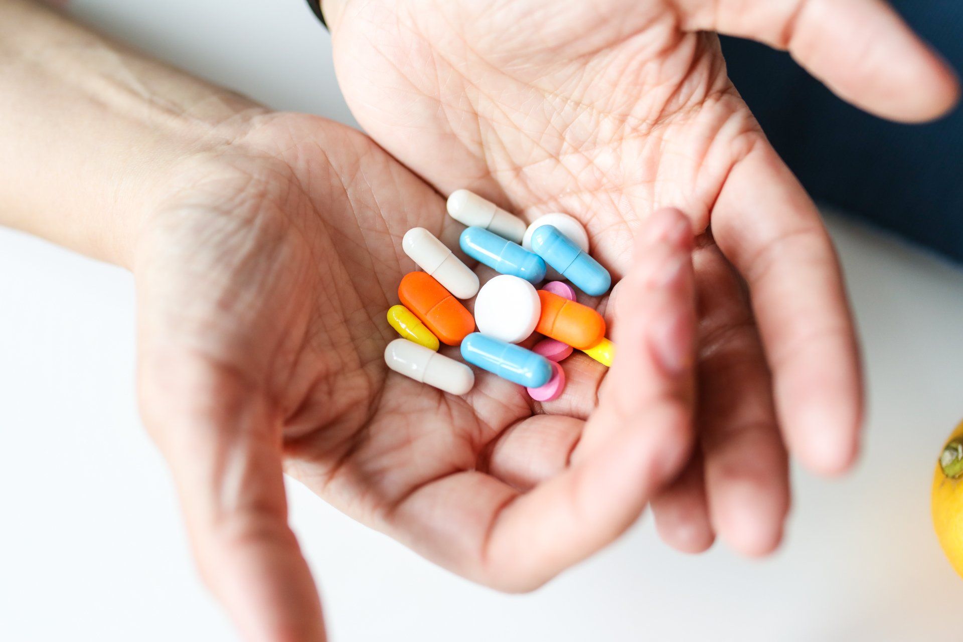 A person's hands holding a variety of colorful pills and capsules.