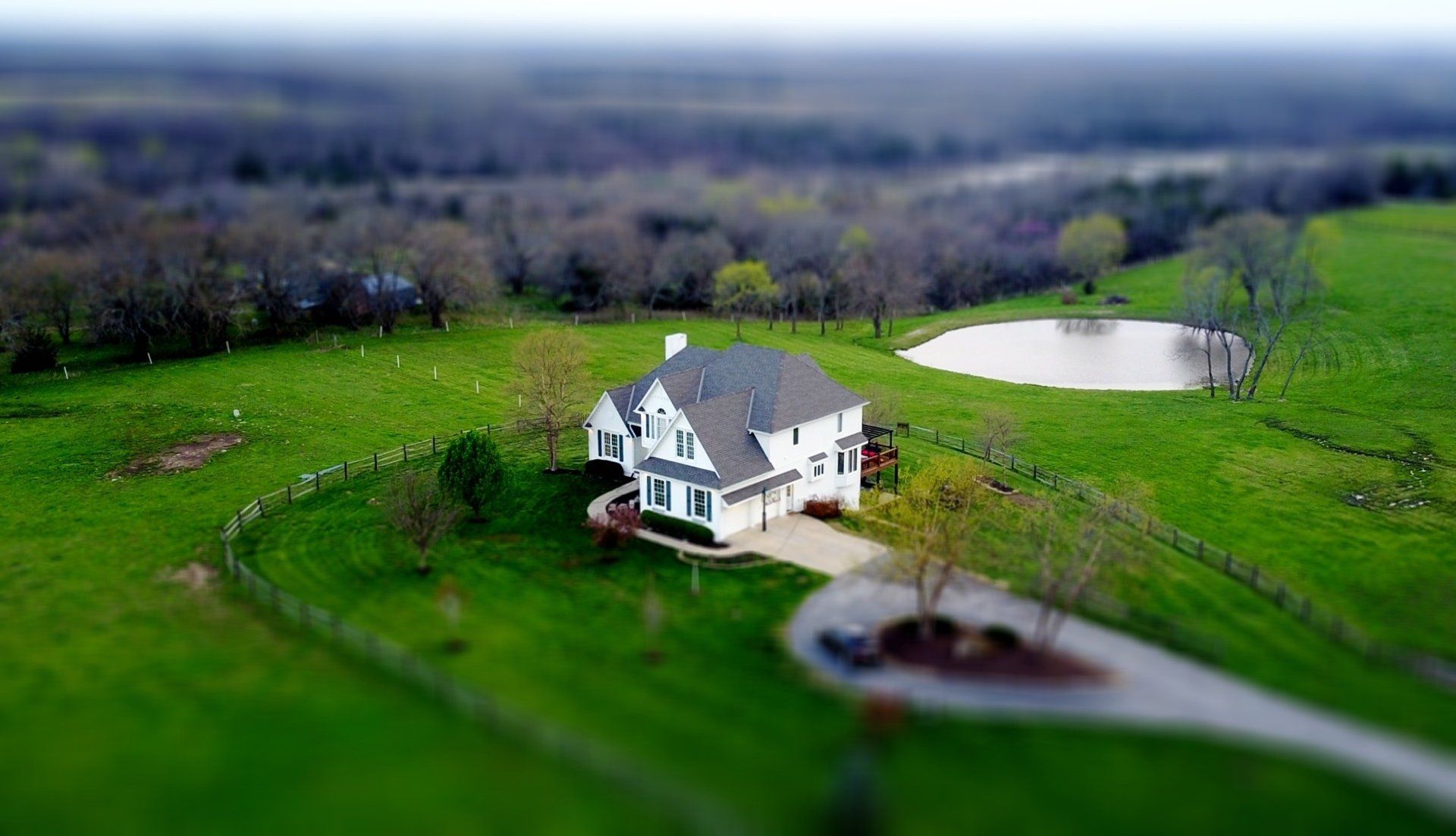 Aerial view of a white house with green lawn and a small pond in a rural landscape.
