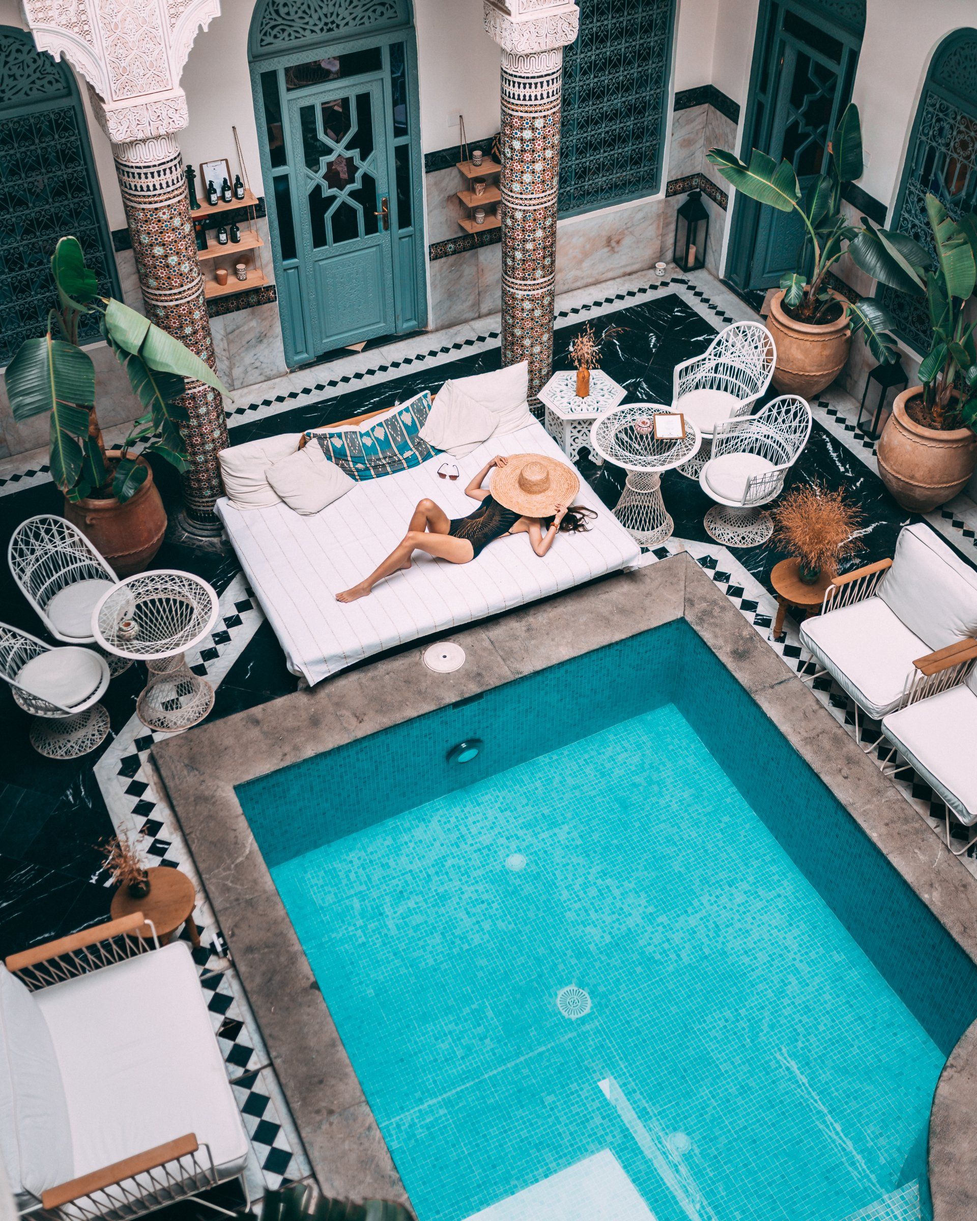 A woman is laying on a couch next to a large swimming pool.