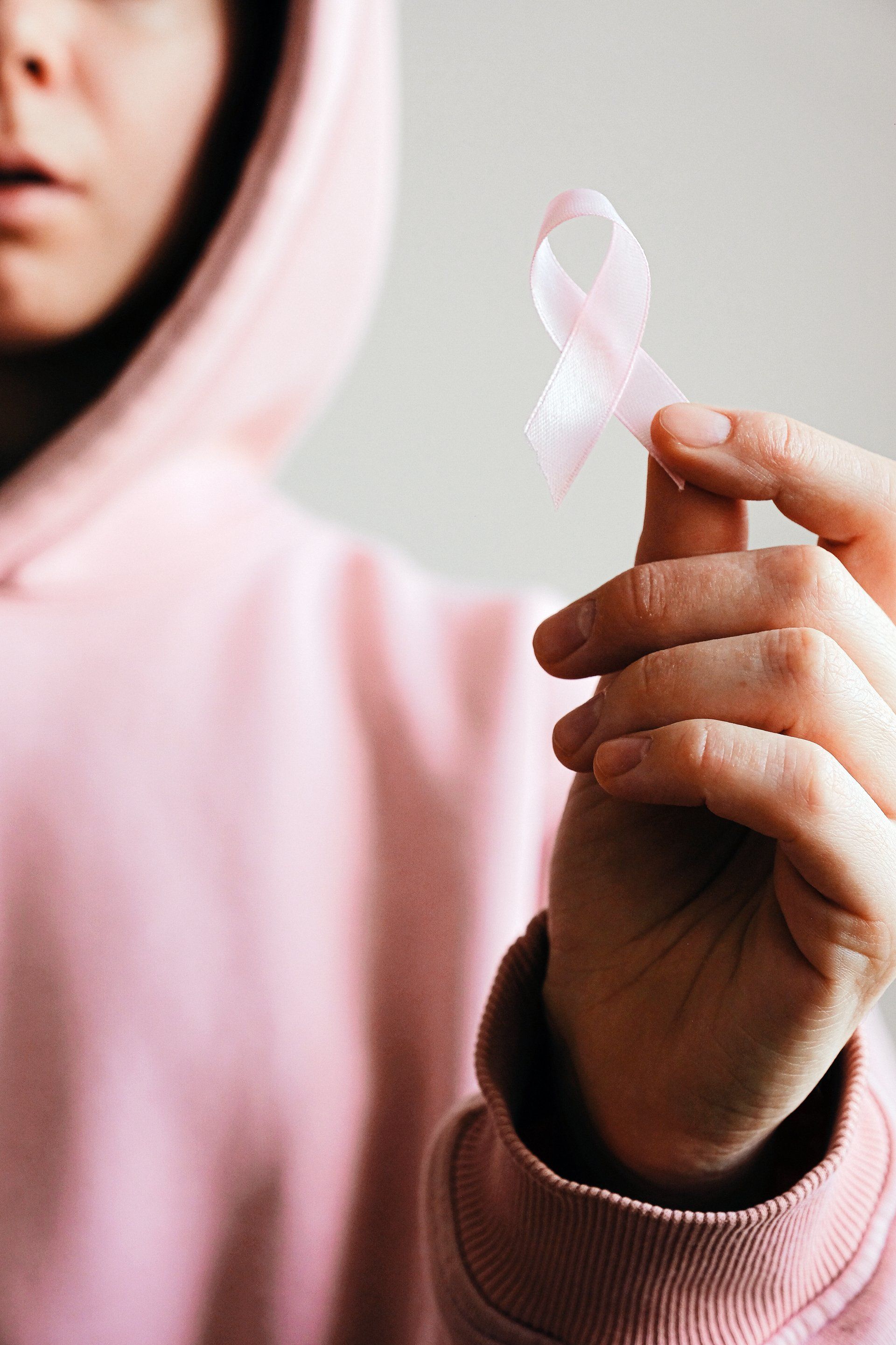 Person in pink hoodie holding a pink ribbon, a symbol of breast cancer awareness.