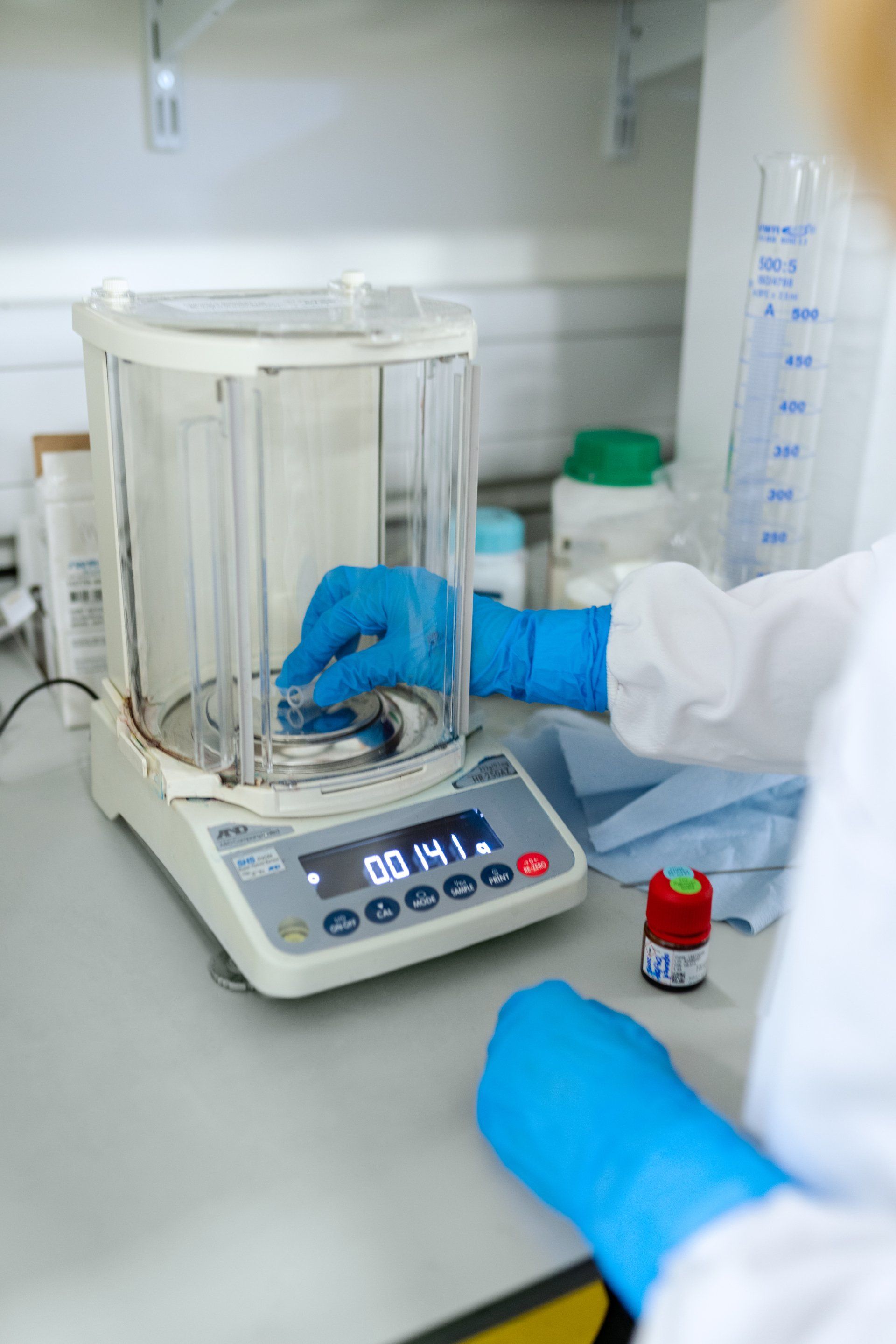 A person wearing blue gloves weighing a substance in a laboratory balance.