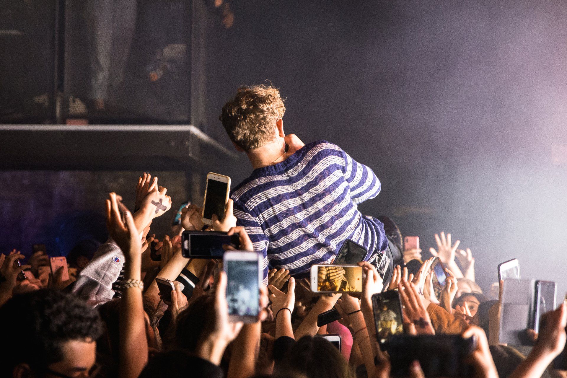 A man in a striped shirt is being lifted by a crowd of people at a concert.