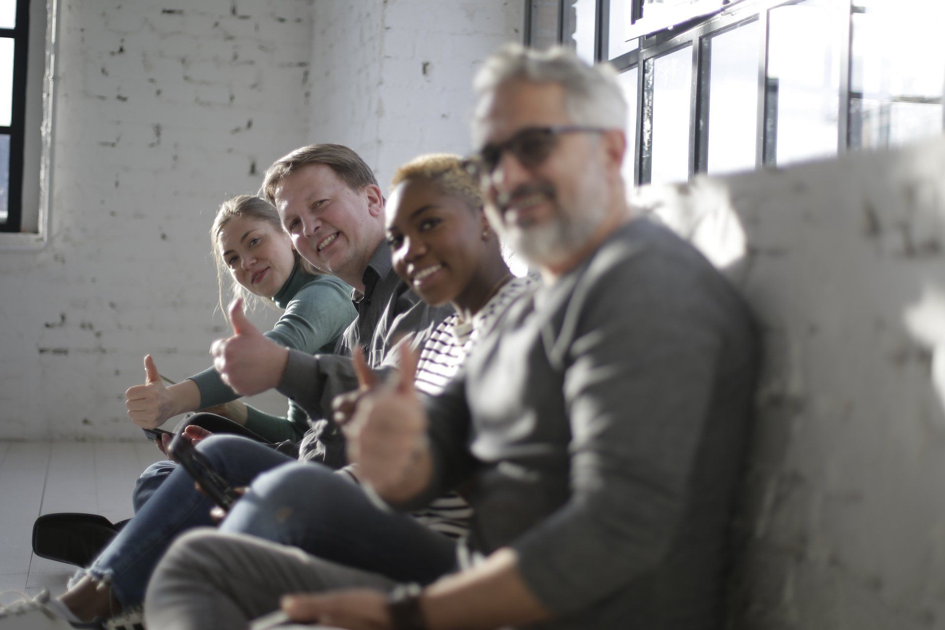People sitting on a couch in a bright room, smiling and giving thumbs up
