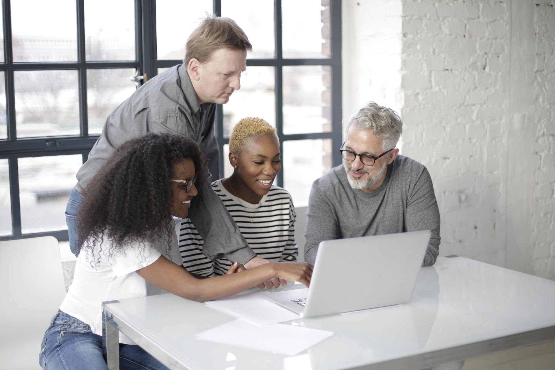 A group of people are sitting around a table looking at a laptop computer.