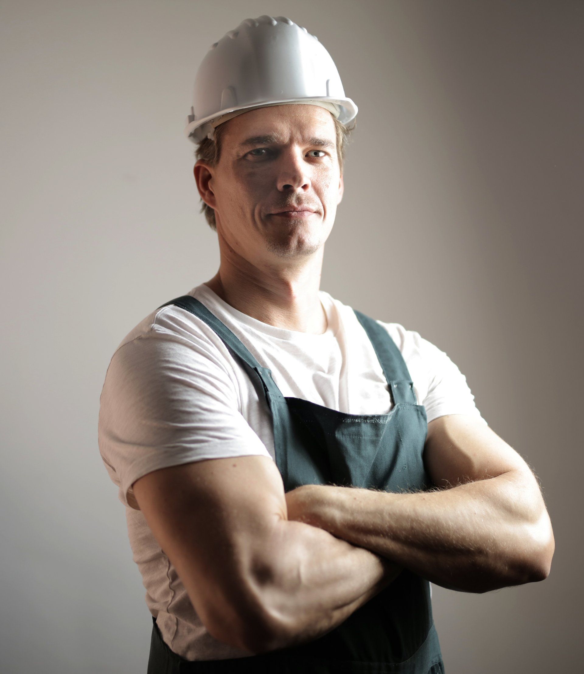 A man wearing a hard hat and overalls with his arms crossed