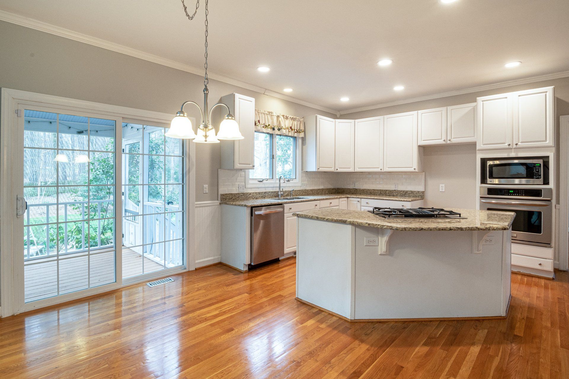 Kitchen with white cabinets, island, and wood floors. Sliding glass door leads to a deck.