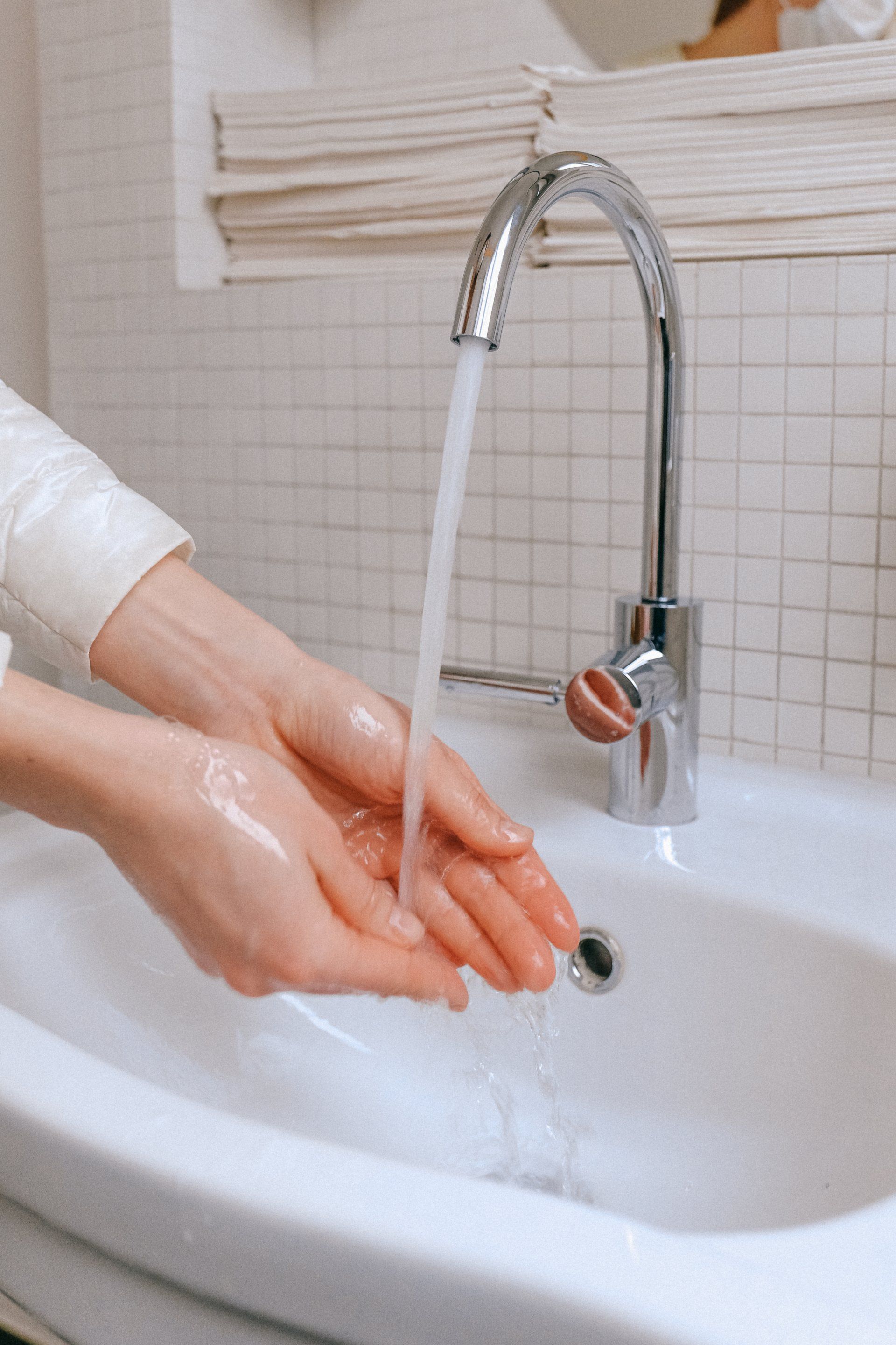 Hands washing under running water in a white sink, near a silver faucet.