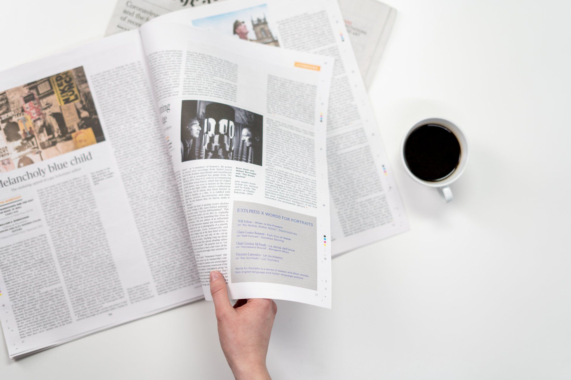 A person is reading a newspaper next to a cup of coffee.