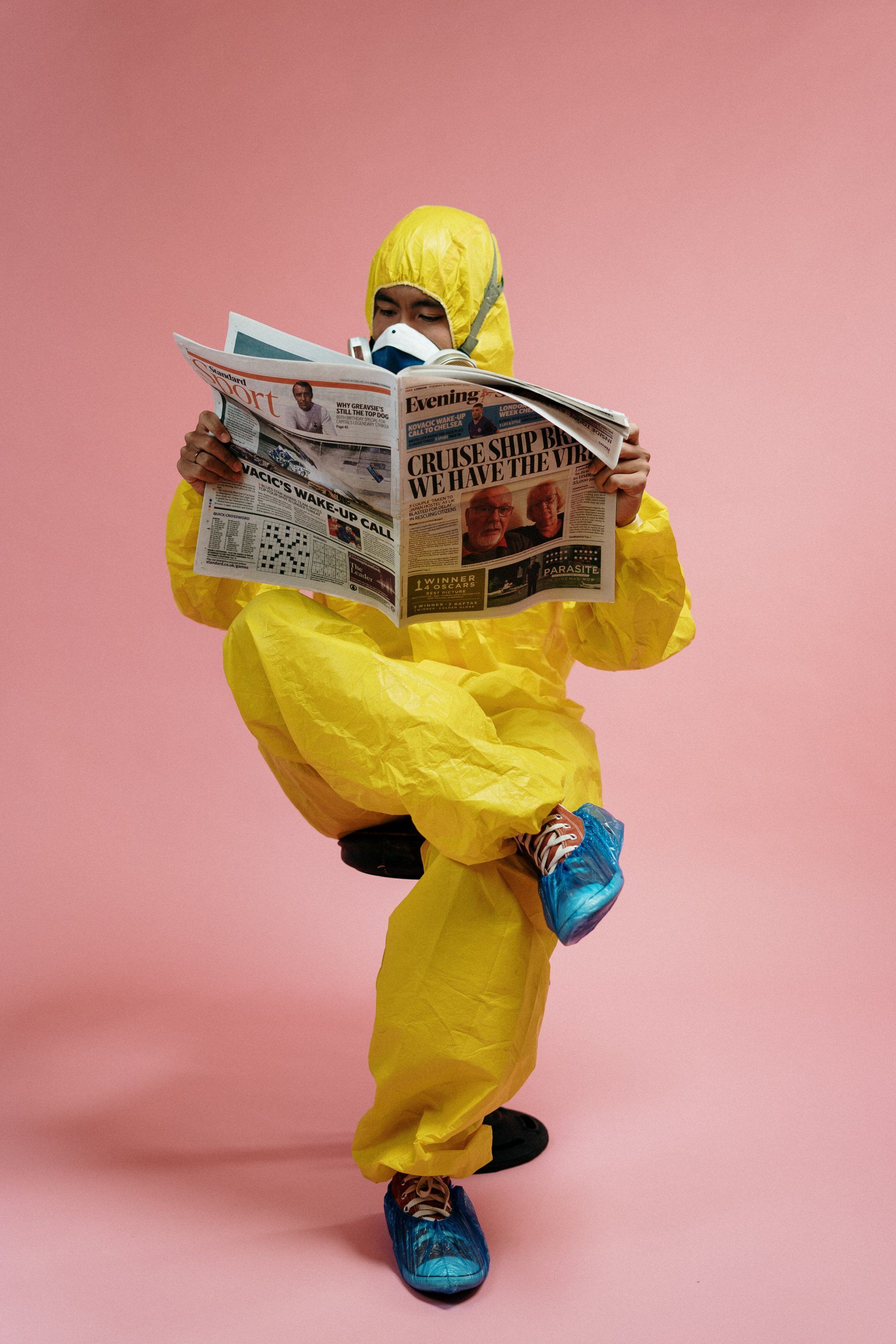 A person in a yellow protective suit is reading a newspaper.