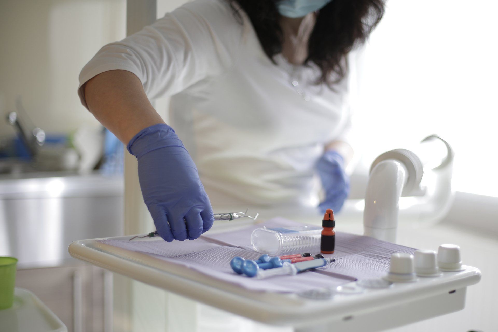 A dentist wearing a mask and gloves is preparing a tray for a patient.