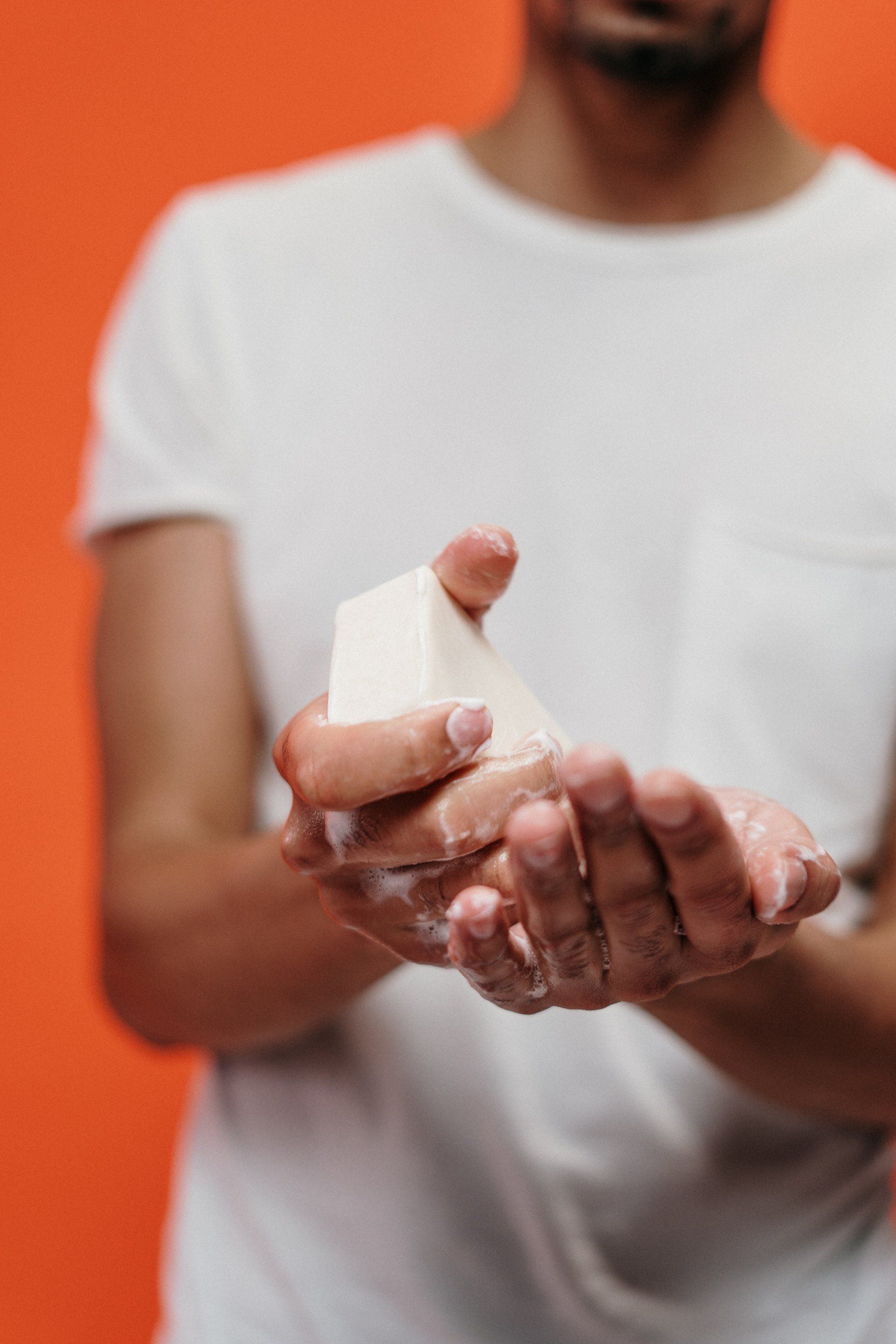 Person in white shirt holding a bandaged hand against an orange background