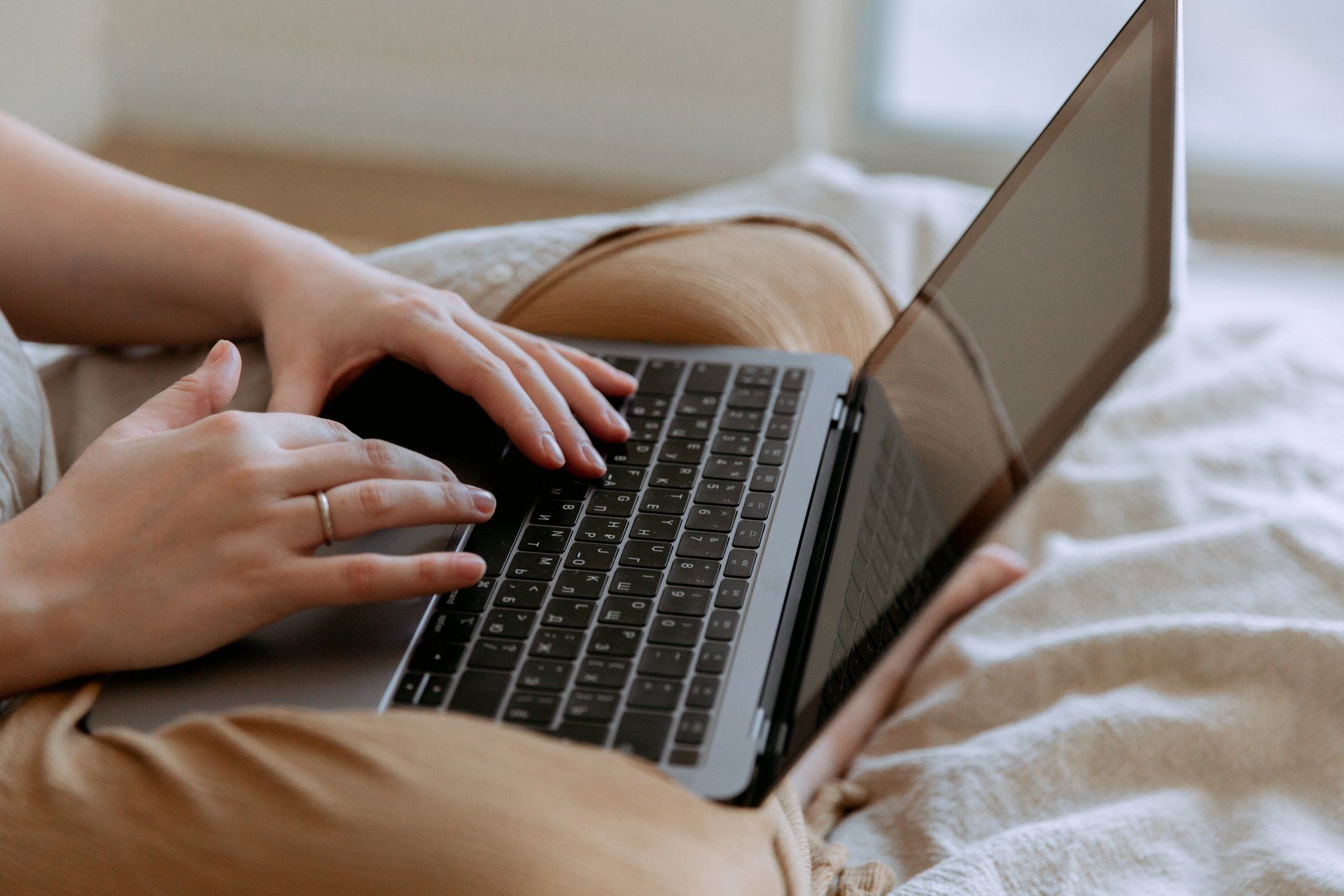 A woman is sitting on a bed using a laptop computer.