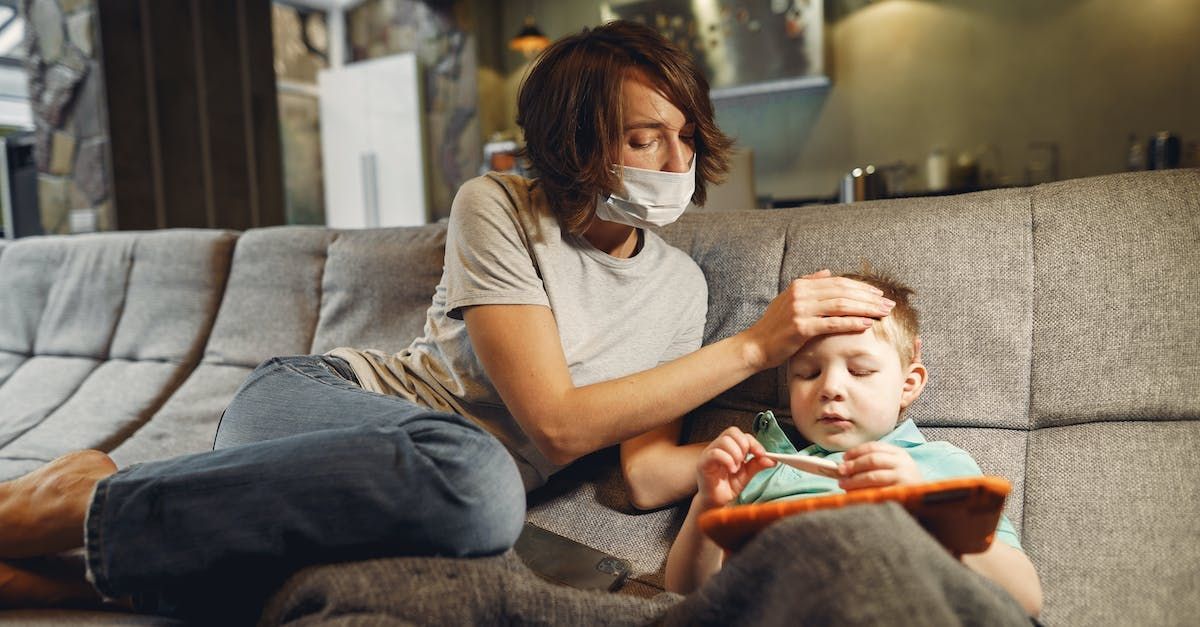 A mother wearing a mask is checking her child's forehead for fever