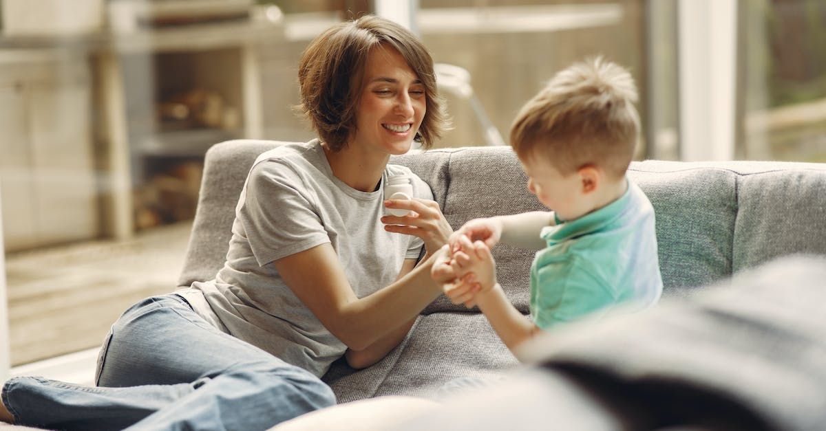 A woman and a child are sitting on a couch holding hands.