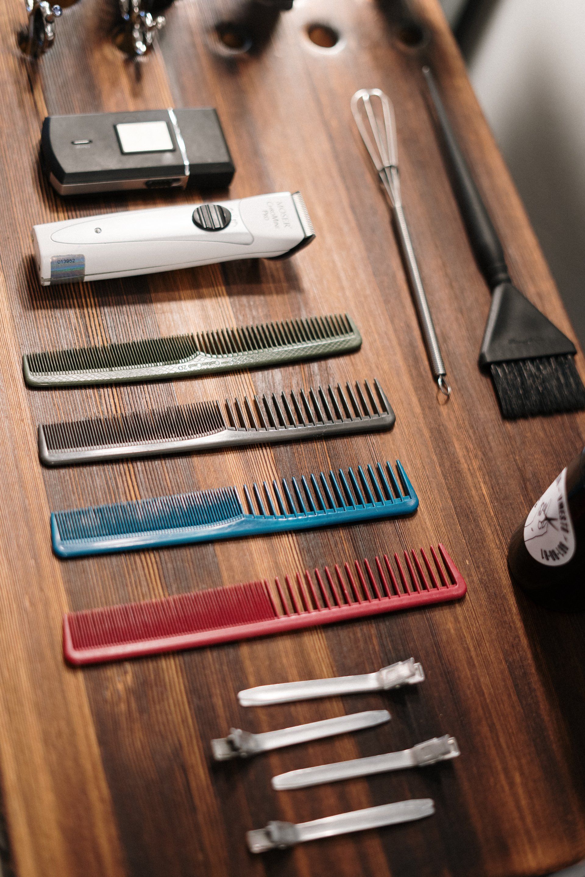 Barber's tools on a wooden surface. Includes clippers, combs of various colors, a brush, and tools.