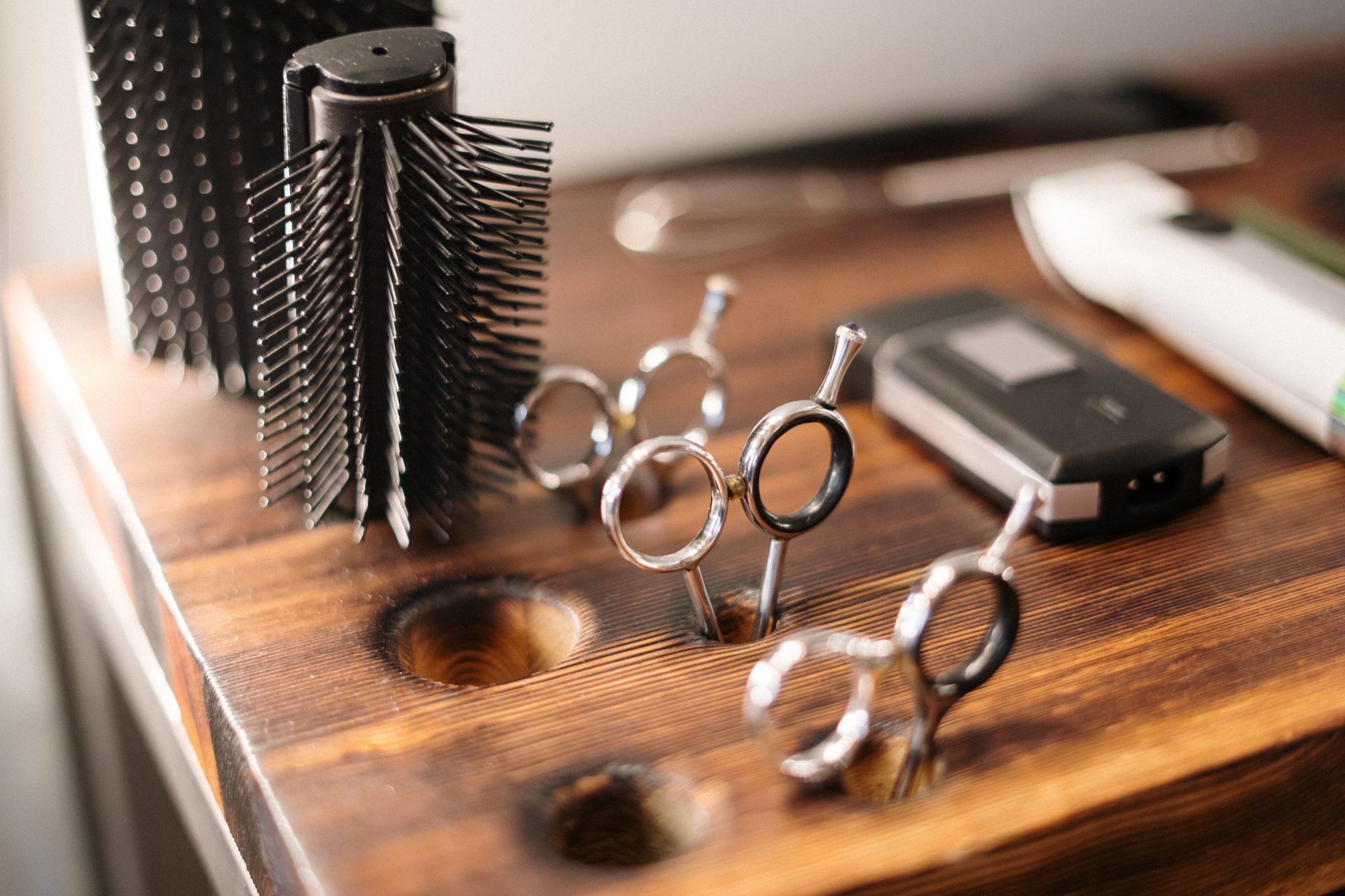 Hairdressing tools on a wooden stand: brushes, scissors, clippers, and comb.