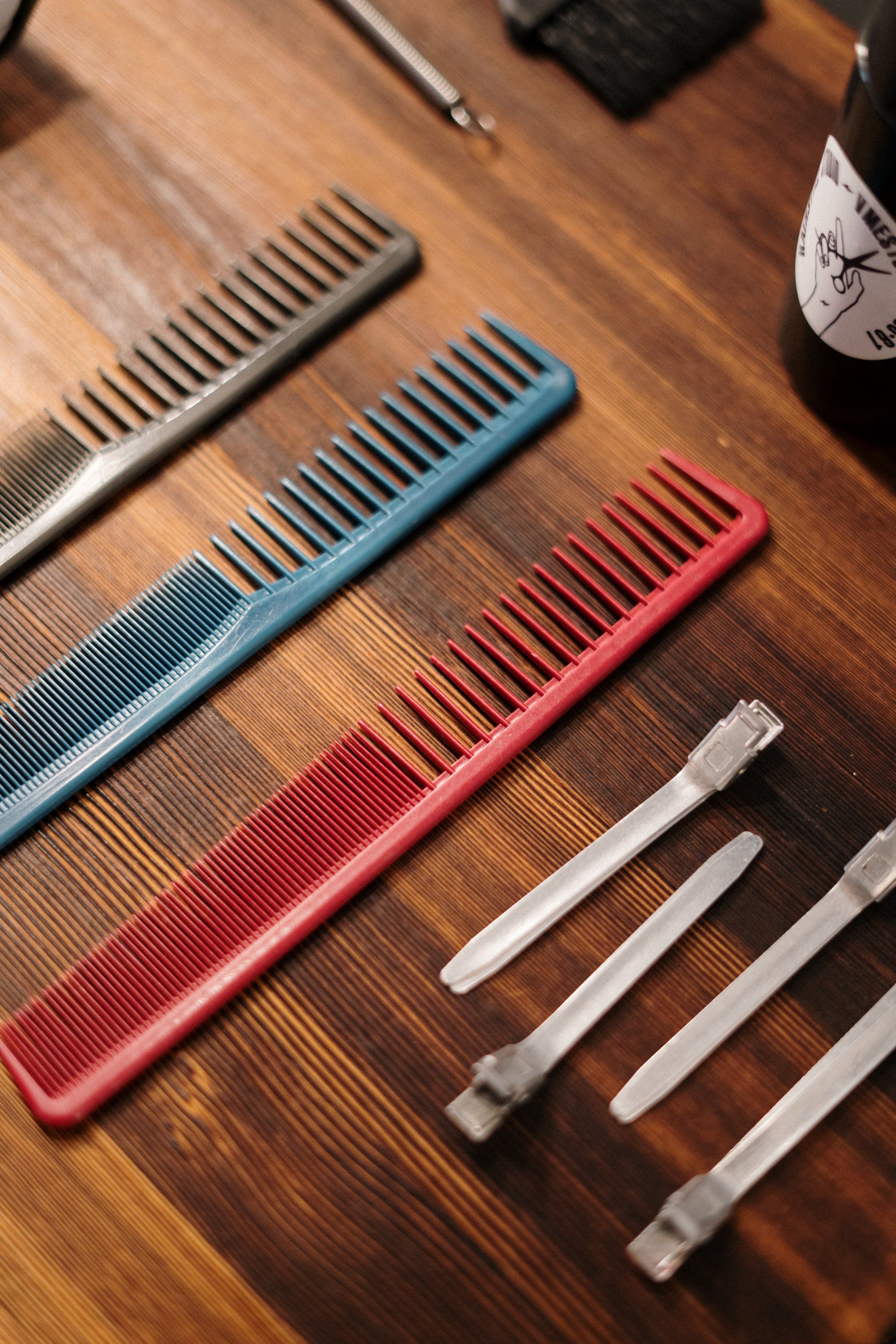 Three combs and cuticle tools on a wood table, in red, blue, and gray.