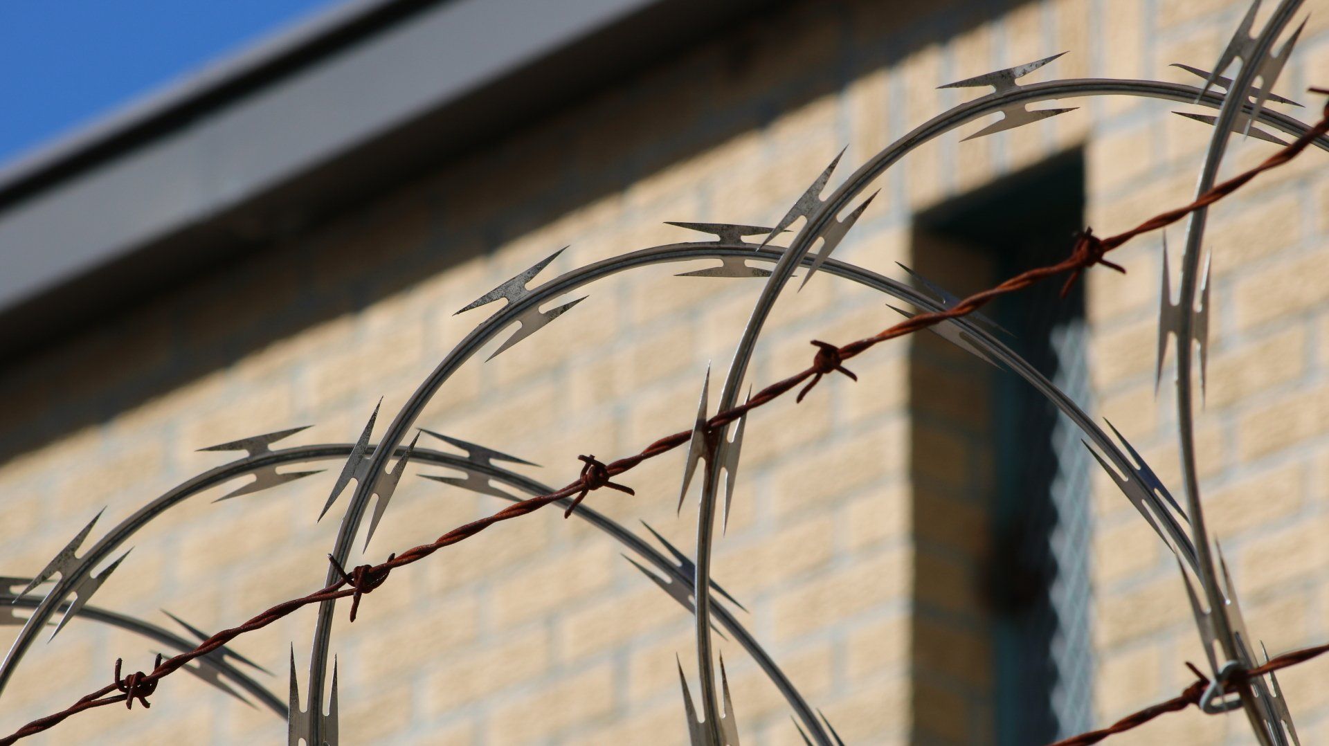 Barbed wire fence in front of a brick building.