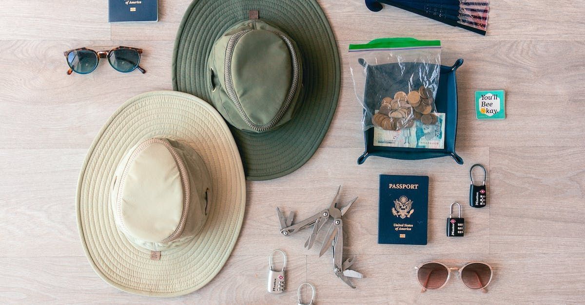A table topped with hats , sunglasses , keys , a passport , and other items.