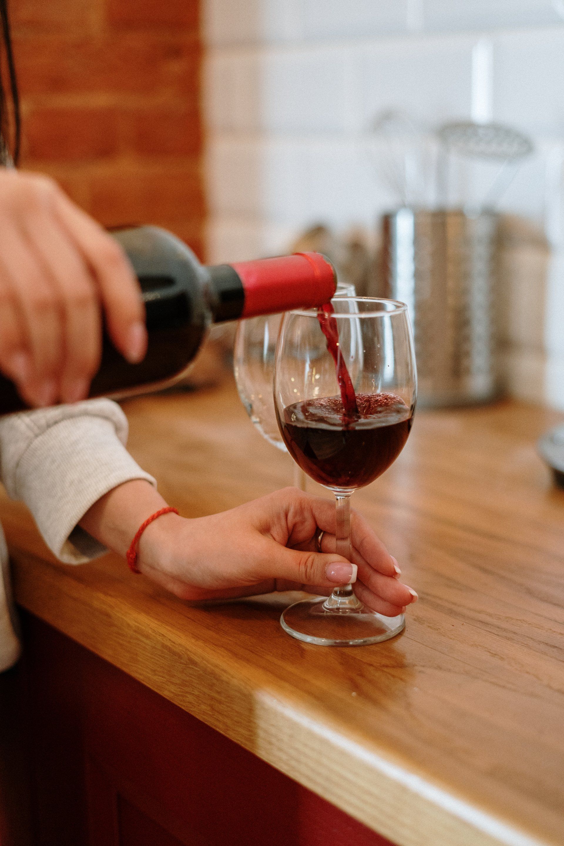A person is pouring red wine into a glass on a wooden counter.