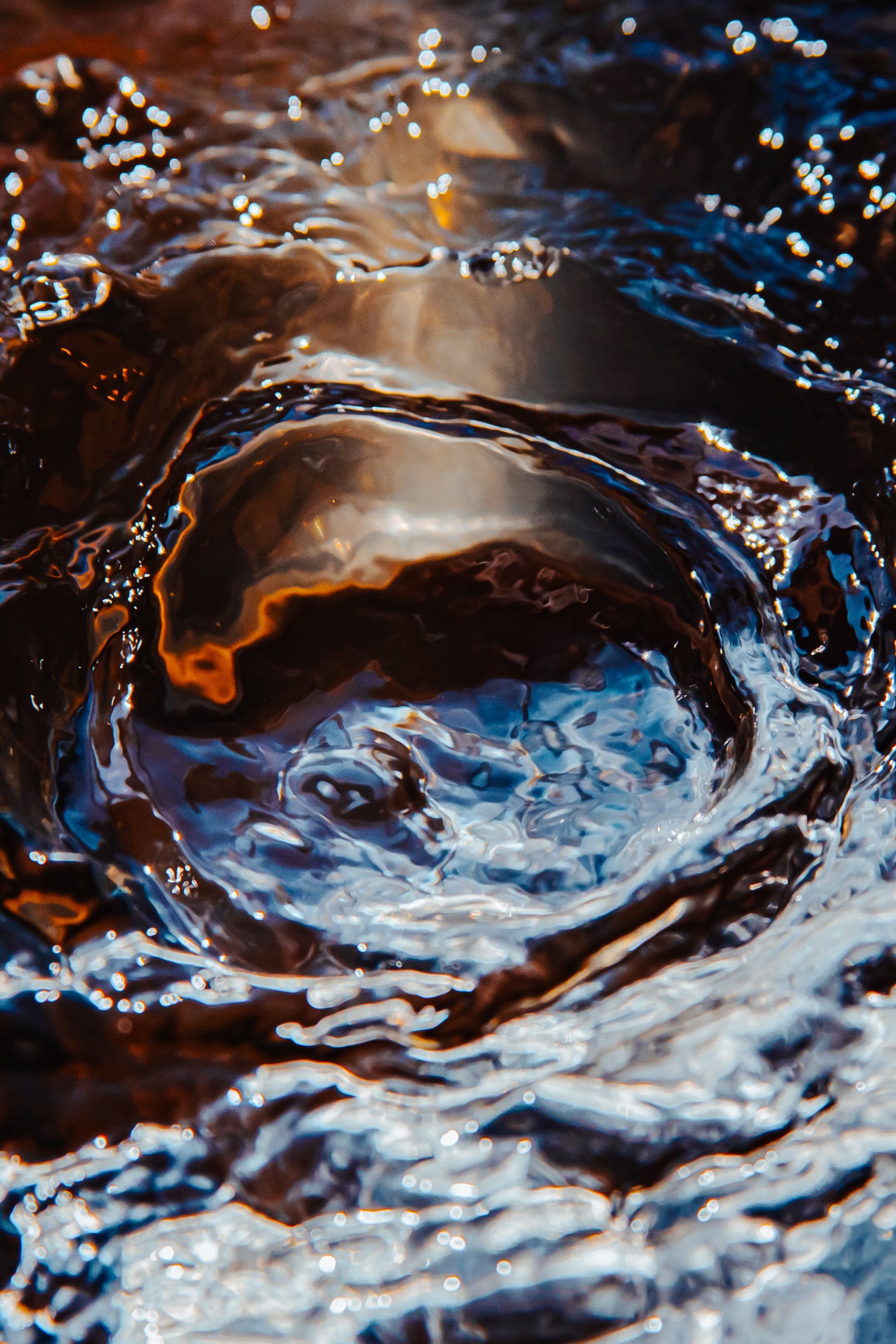 Water surface rippling with light reflections; swirling blues, browns, and golds.